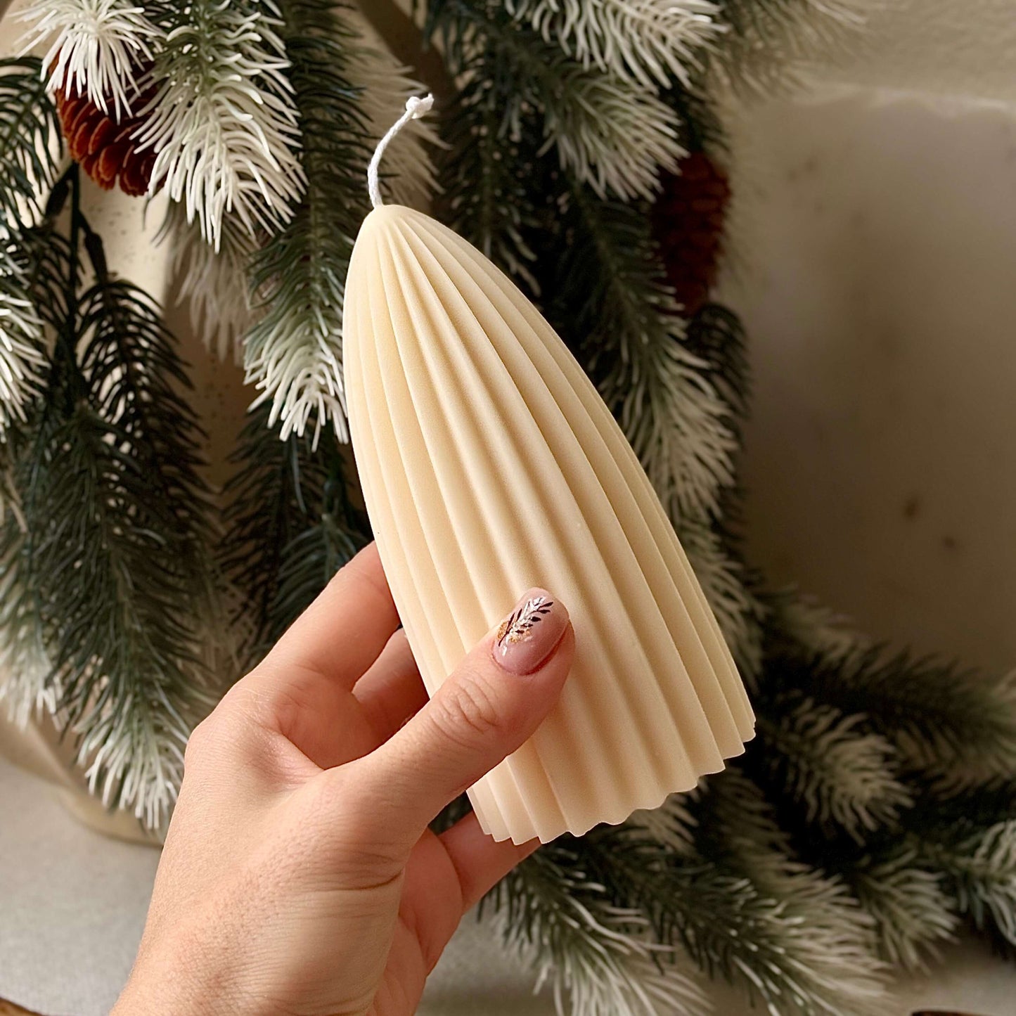 Hand holding ivory ribbed soy candle in Christmas tree shape, artisan holiday decoration piece