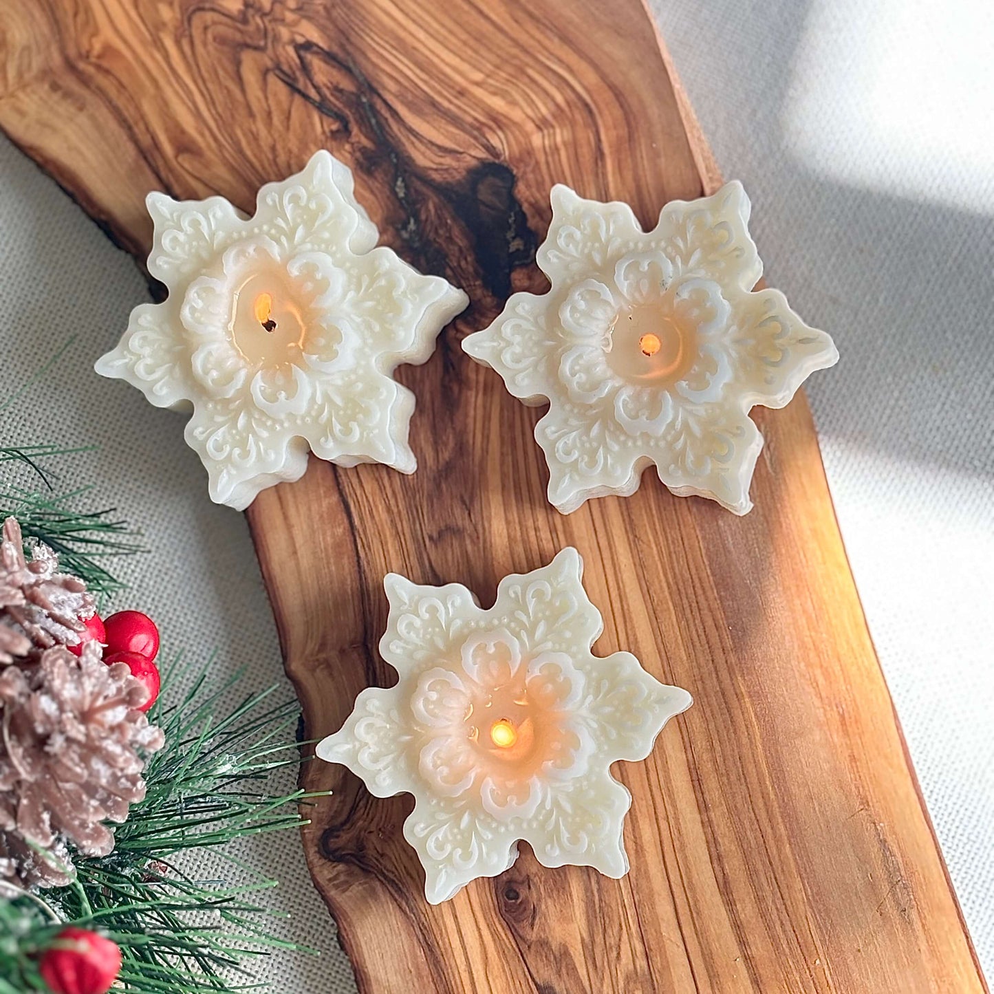 Burning snowflake shaped candle on wood tray with holiday greenery