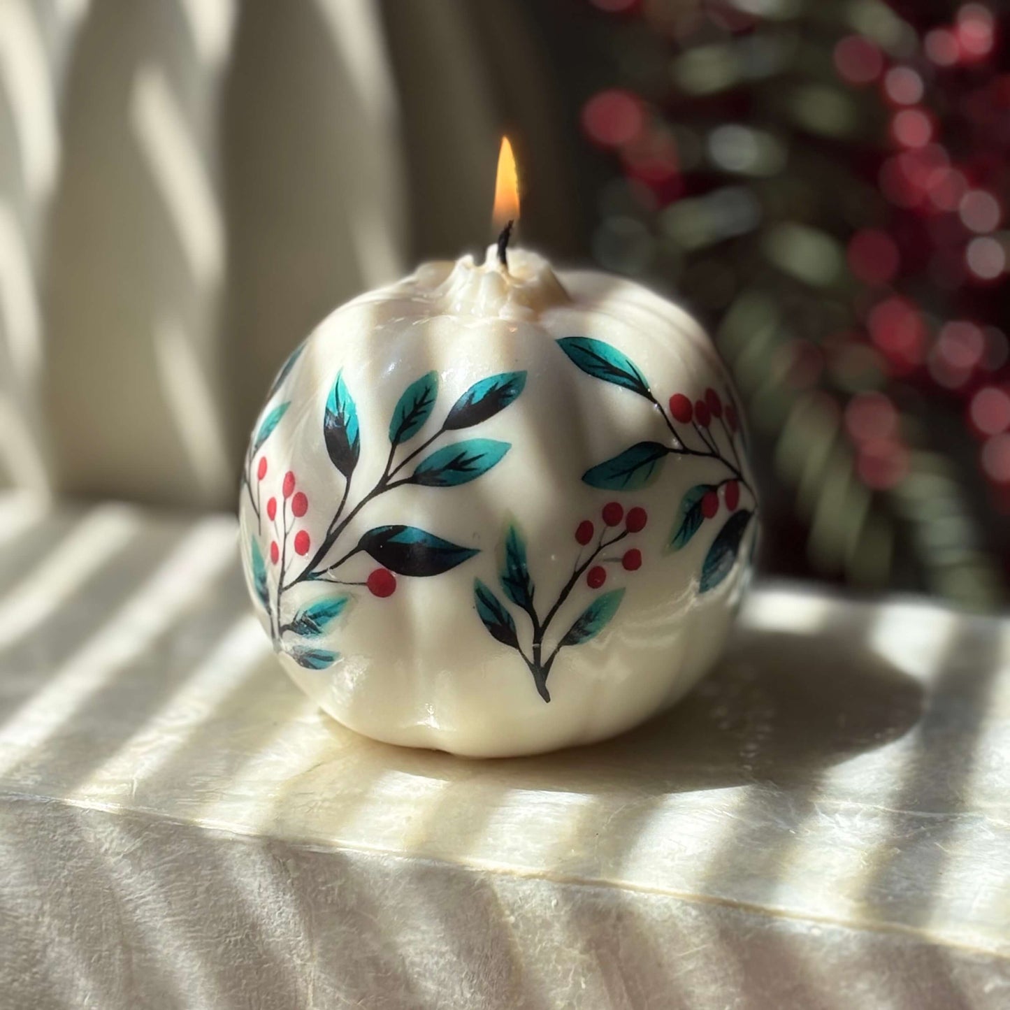 Glossy floral pumpkin candle with teal leaves and red berries burning on a marble surface, perfect as Halloween home accent, fall decor or Thanksgiving hostess gift