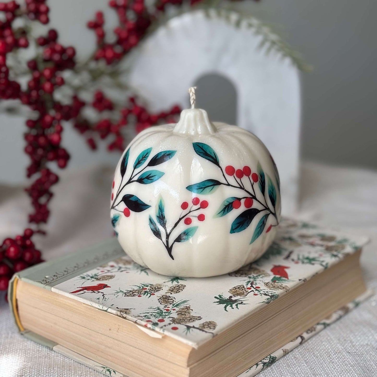 Decorative pumpkin-shaped candle with floral and berry design, placed on a festive holiday book — perfect handmade gift for Thanksgiving, Christmas, Halloween or fall birthday