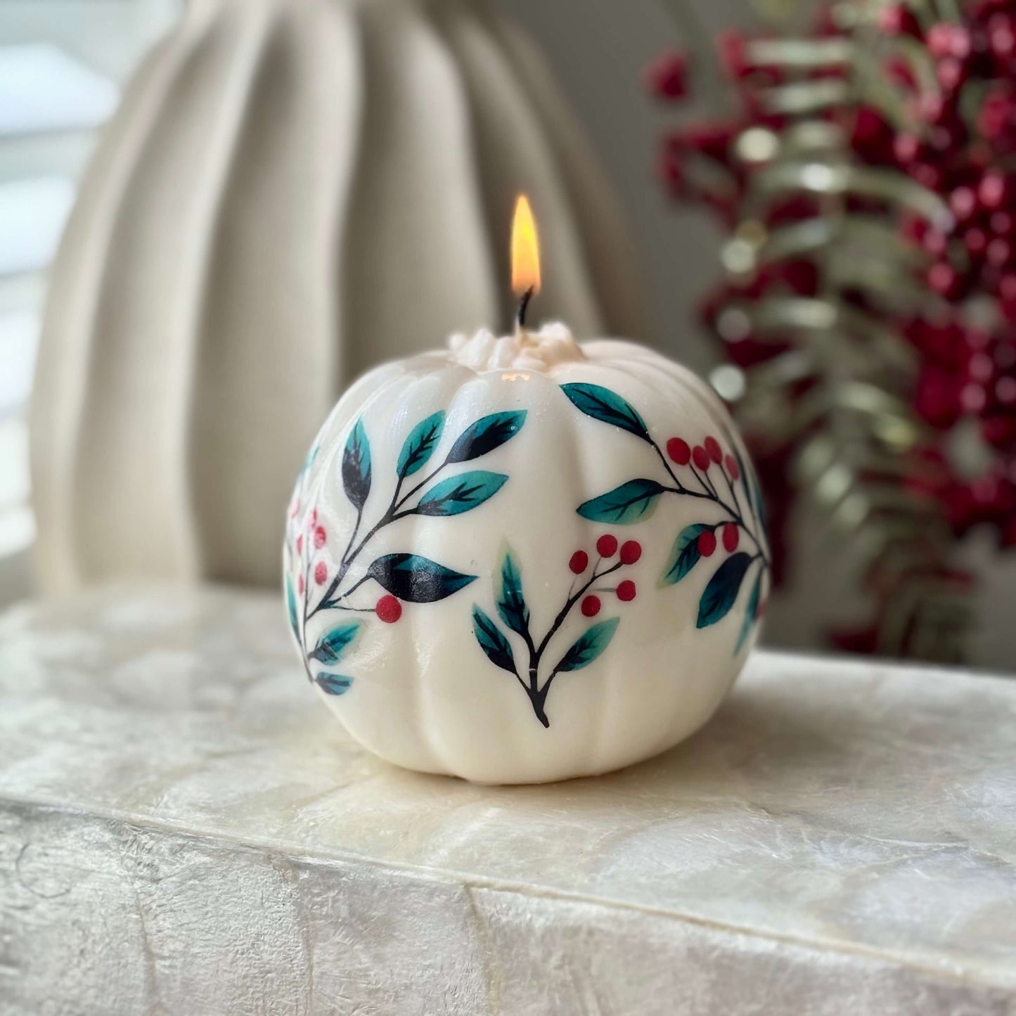 Lit vintage-style pumpkin candle with teal leaves and red berries on a soft textured surface — cozy fall decor for Halloween, Thanksgiving, Secret Santa or housewarming