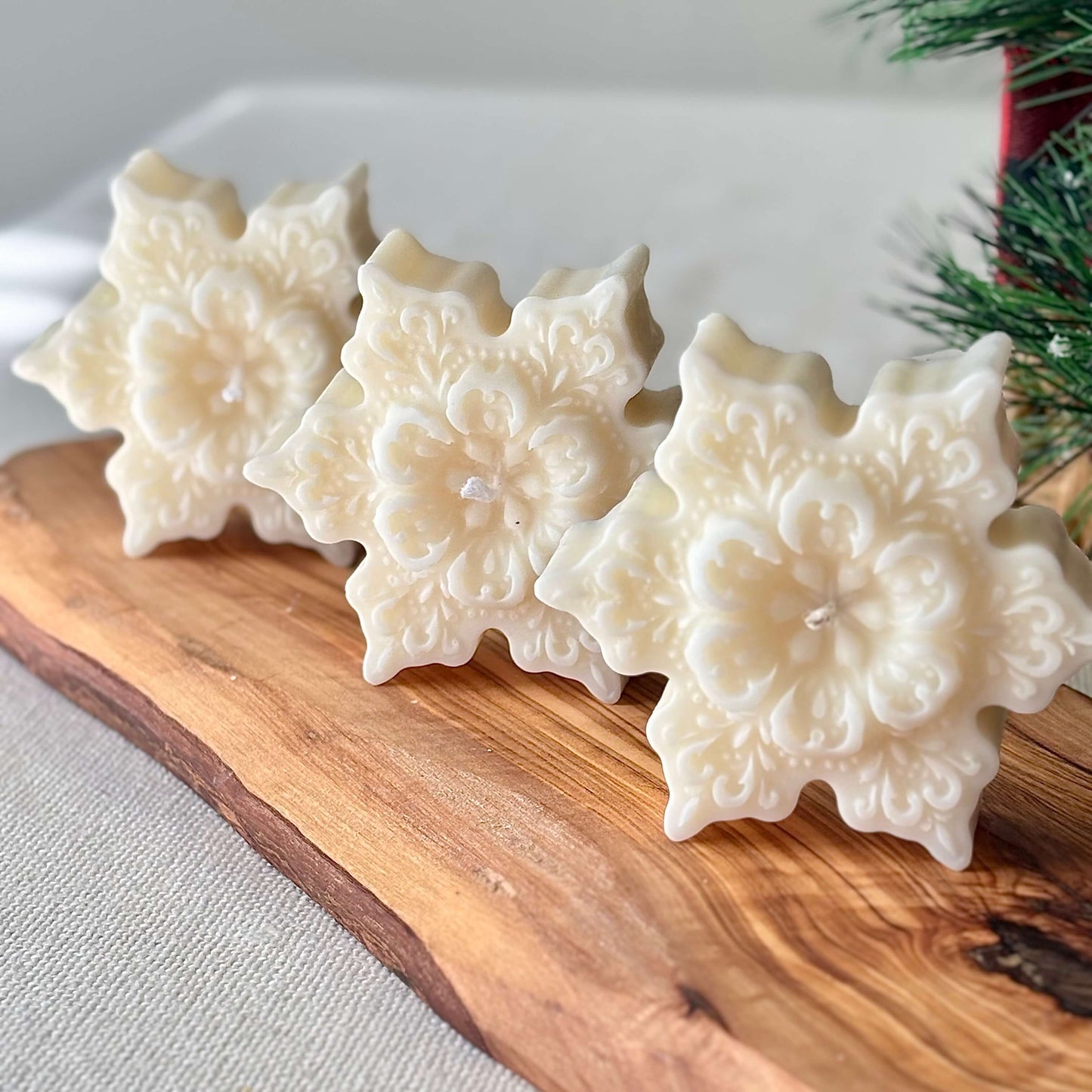 Three handmade snowflake soy candles with floral pattern on a wooden board