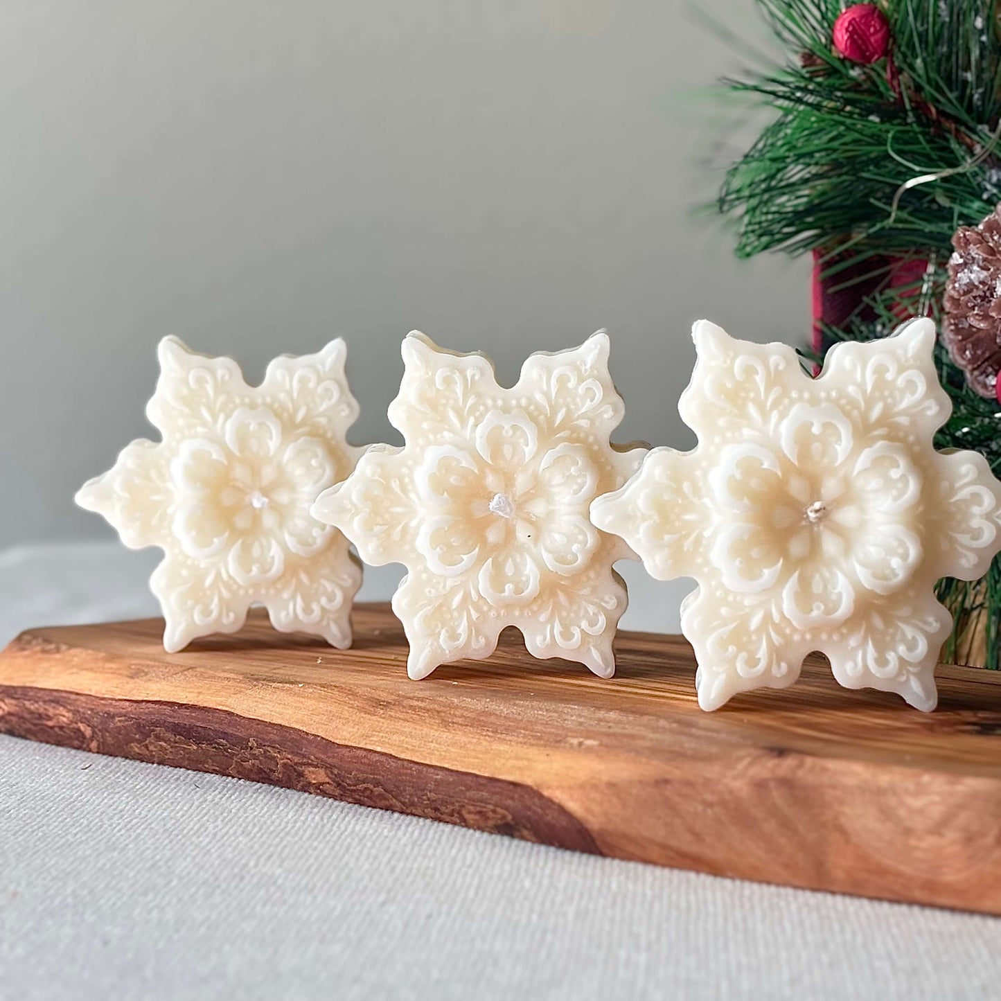 White snowflake candles displayed on wooden tray with pine and holiday berries