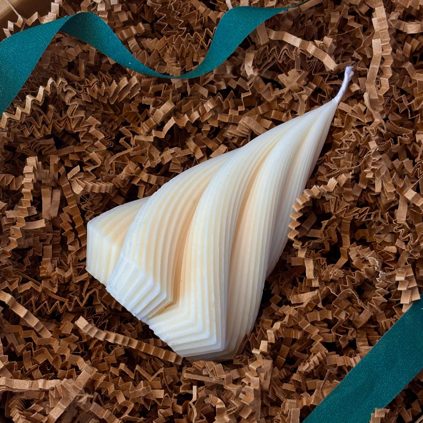 Ivory twisted tree-shaped soy candle on festive shredded paper with blue ribbon for holiday gift packaging