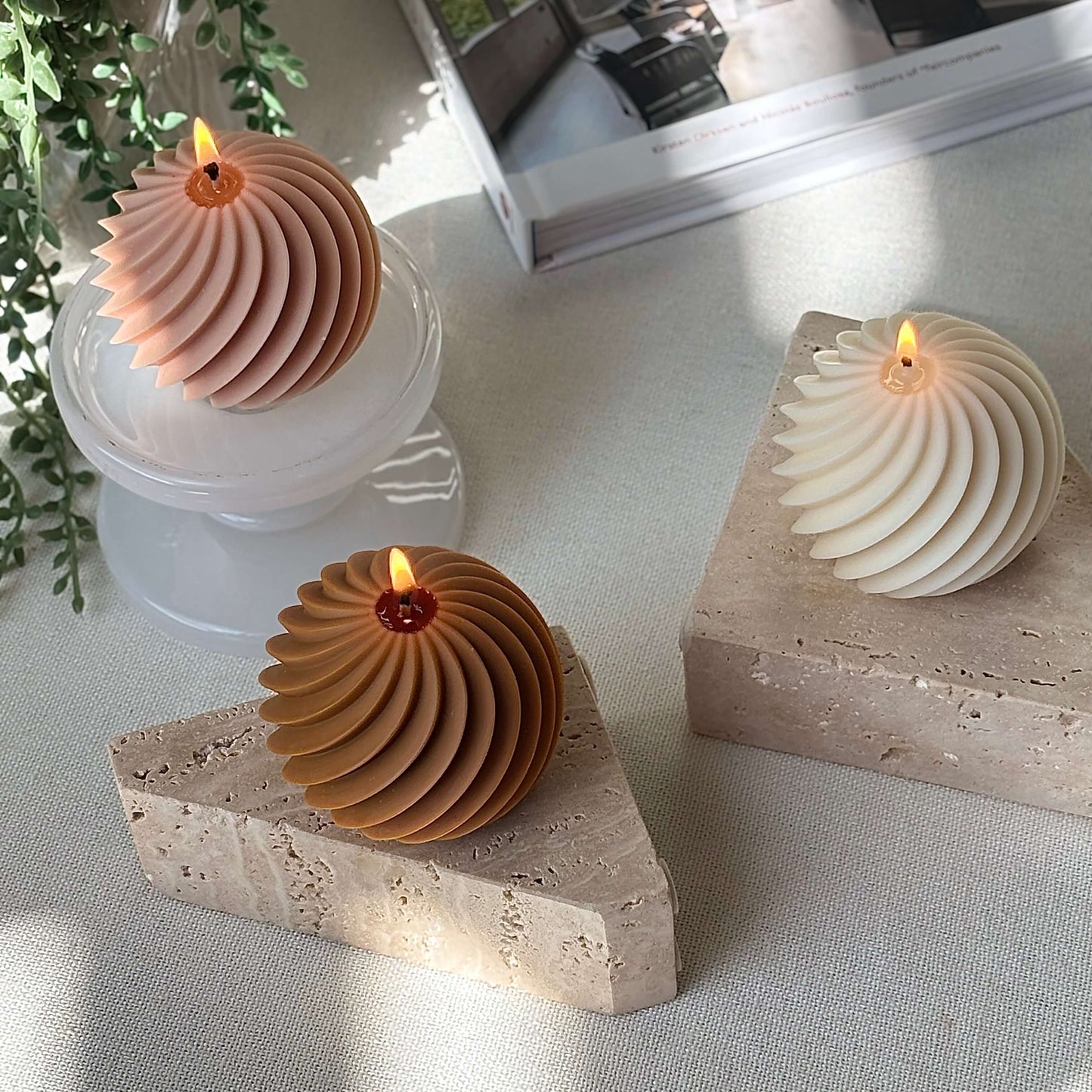 Three burning spiral sphere candles in peach, ivory and honey colors on marble and stone bases, cozy home gift decor.