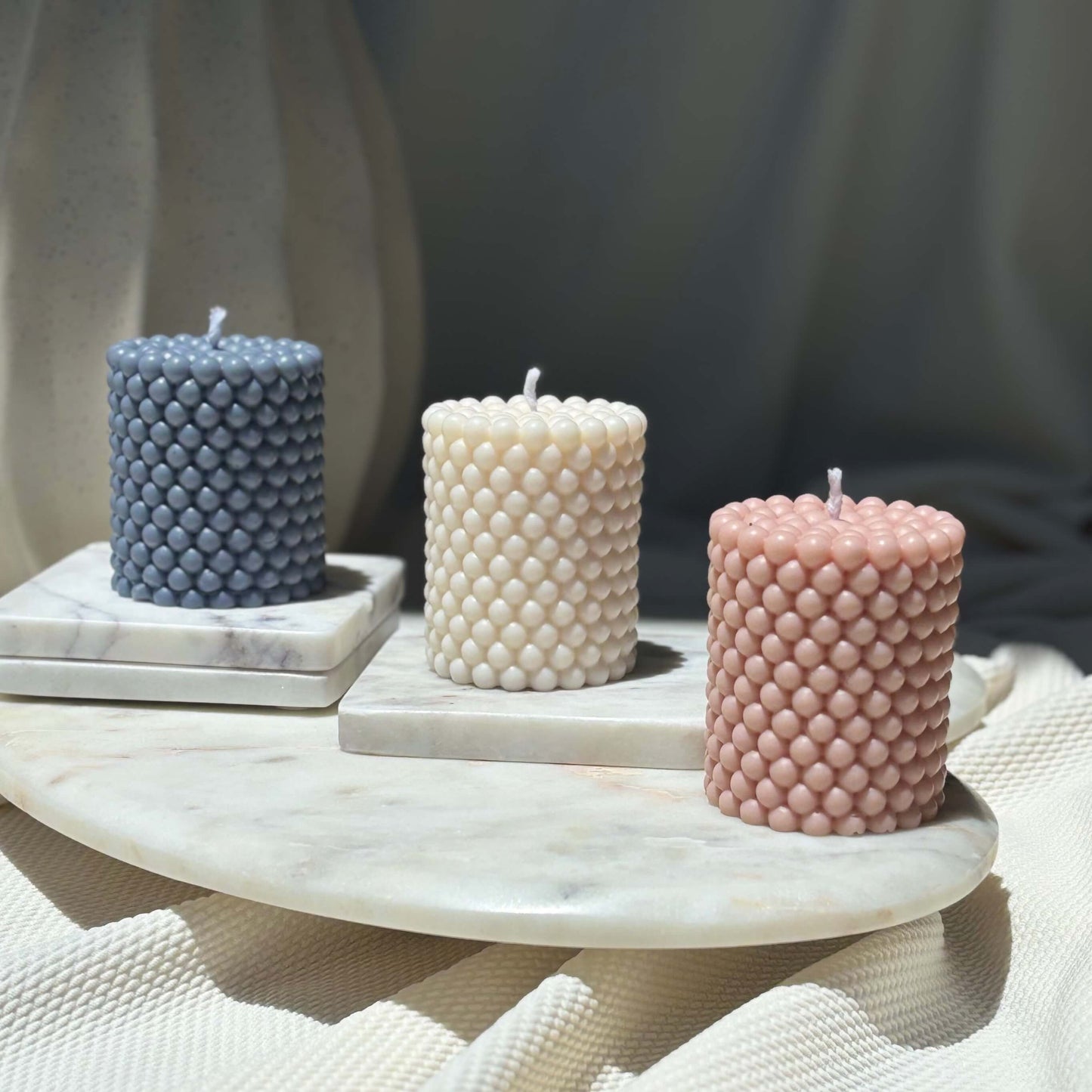 Three sculpted wax pillars in soft natural colors — handmade gift-ready candles for warm interiors.