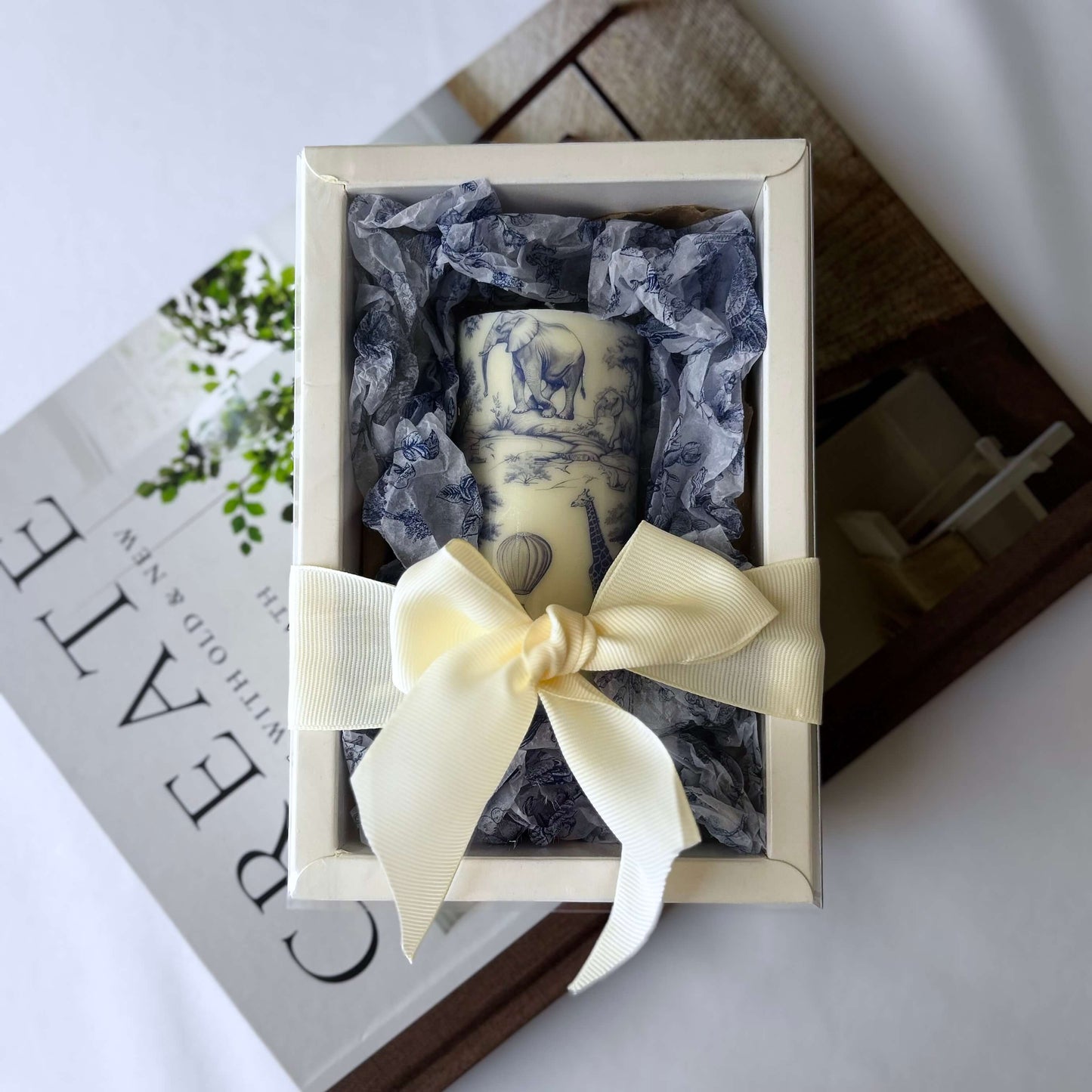Handmade glossy Toile de Jouy candle in elegant gift box with bow, styled for coffee table or Afro-inspired home décor.