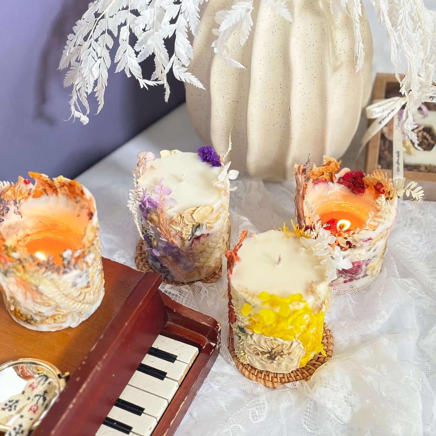 Charming set of botanical soy candles in warm orange, soft purple, and yellow floral tones, with vintage props — two candles lit, ideal for gifting or cozy decor.