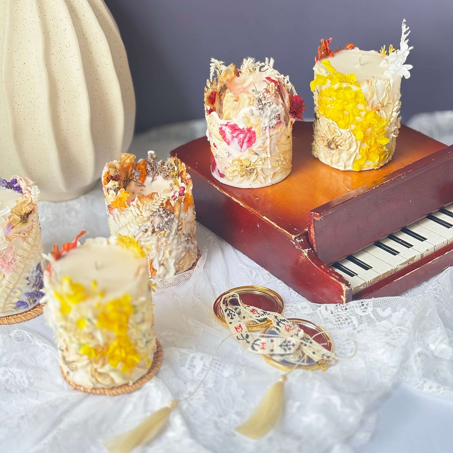 Vintage-style arrangement of handmade botanical soy candles with dried flowers in yellow, red, and purple accents — artisan decor and perfect gift idea.