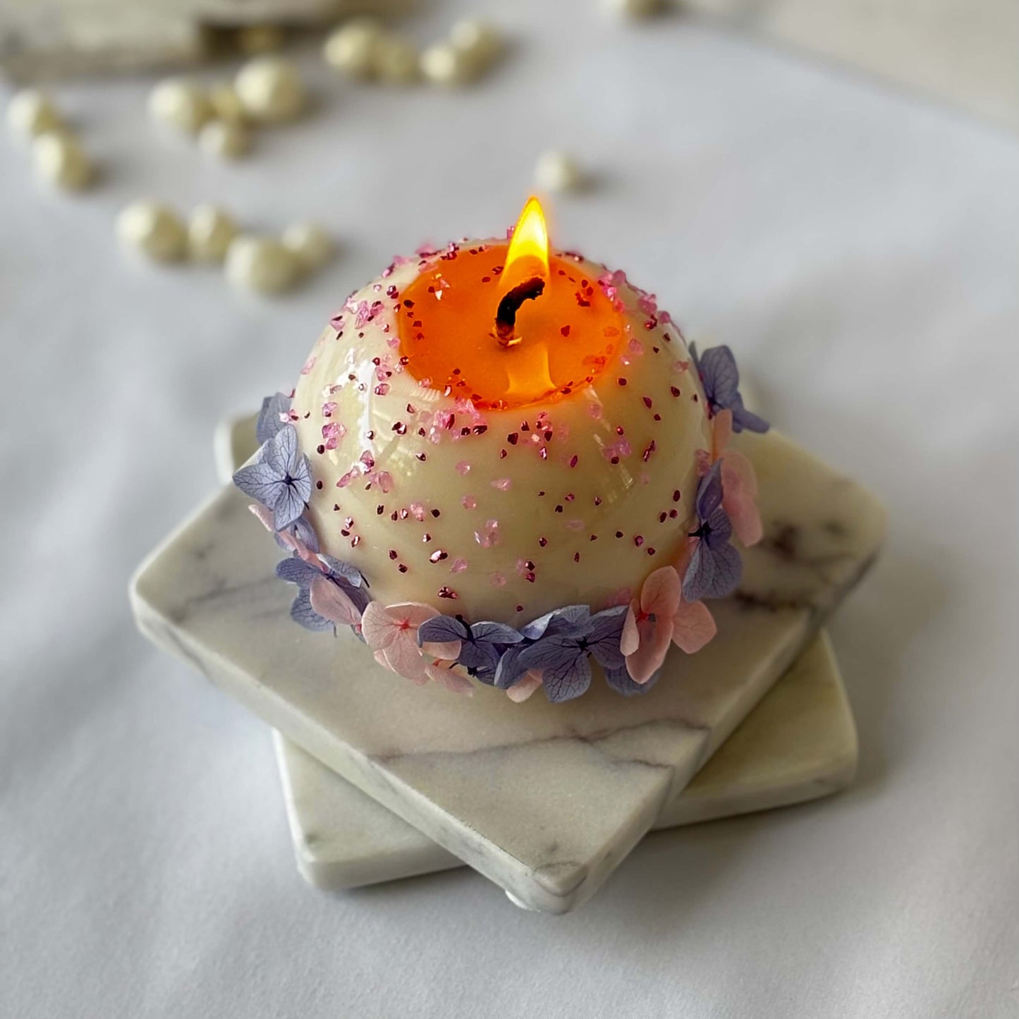 Burning floral soy wax candle with pink sprinkles and pastel hydrangea petals on marble tray
