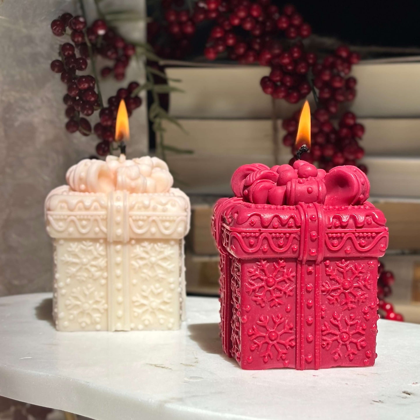 Two decorative gift box candles, one red and one white, glowing with festive flames.