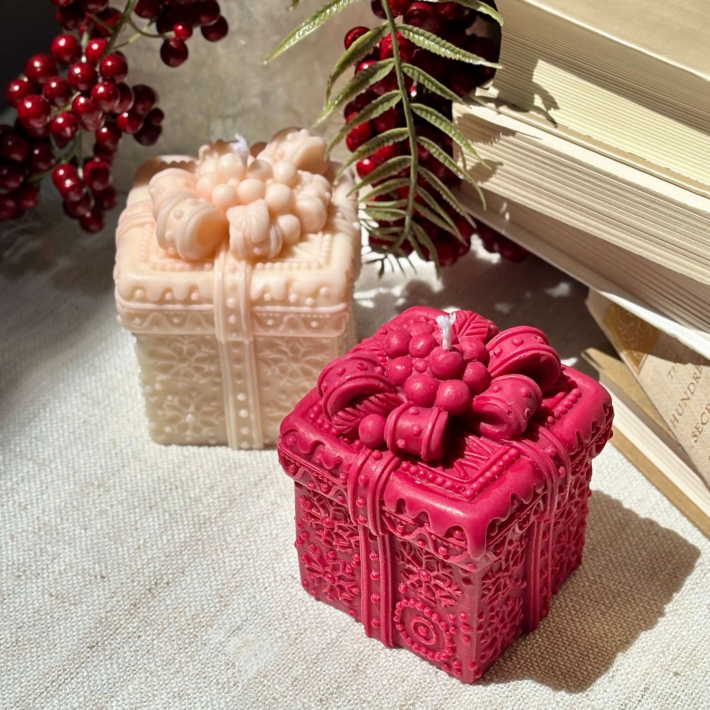Red and beige decorative gift box candles styled with holiday berries and books for festive decor.