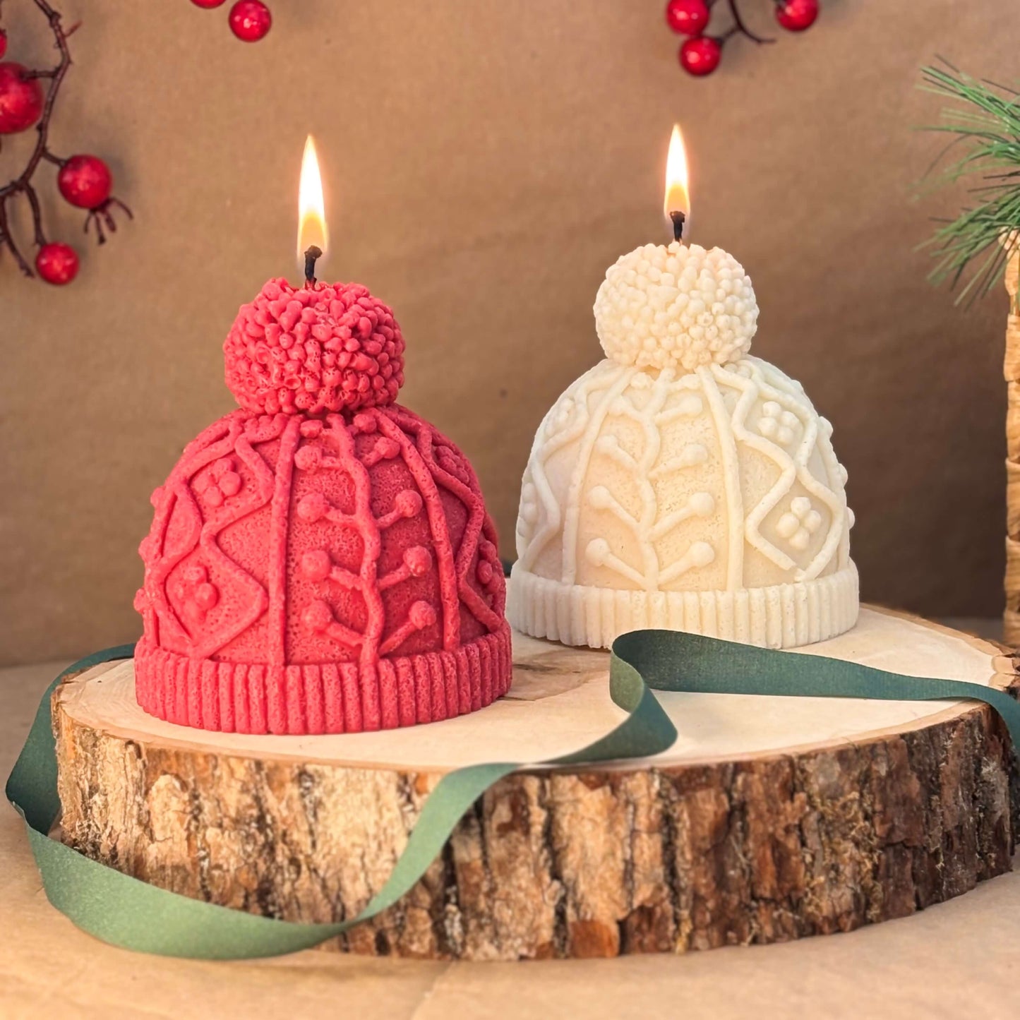 Red and white soy candles shaped like knit winter hats displayed on a wood slab with holiday ribbon for Christmas table decor and festive gift idea