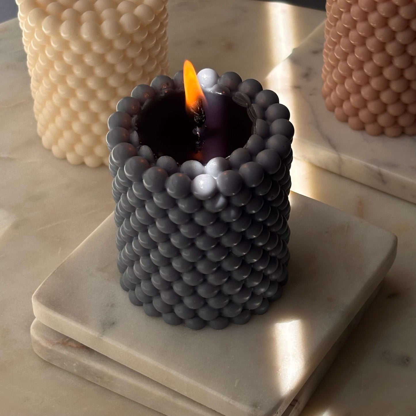 Burning charcoal-toned candle with pearl texture — soy wax sculpture with moody glow on marble.
