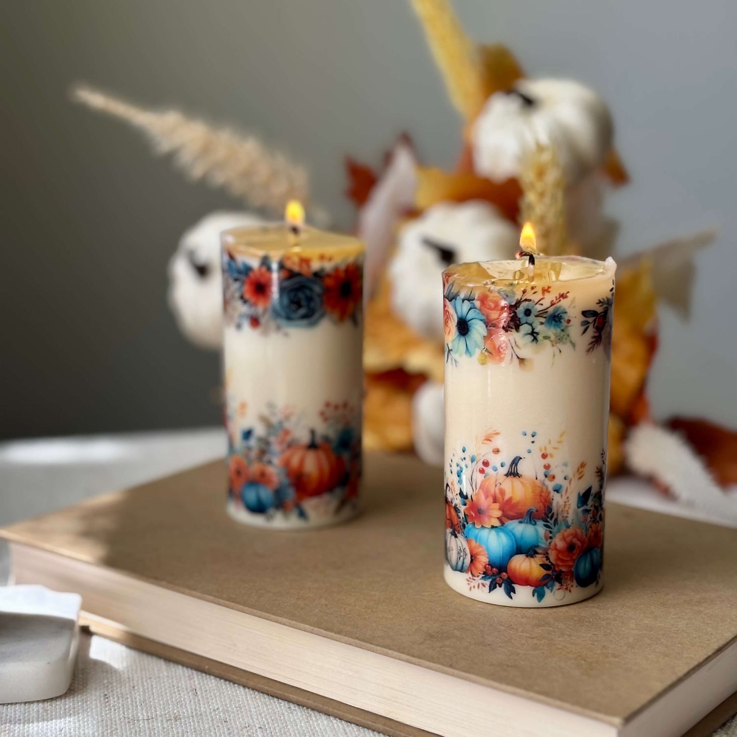 Two diamond glossy pumpkin candles with floral autumn design on wooden book surface