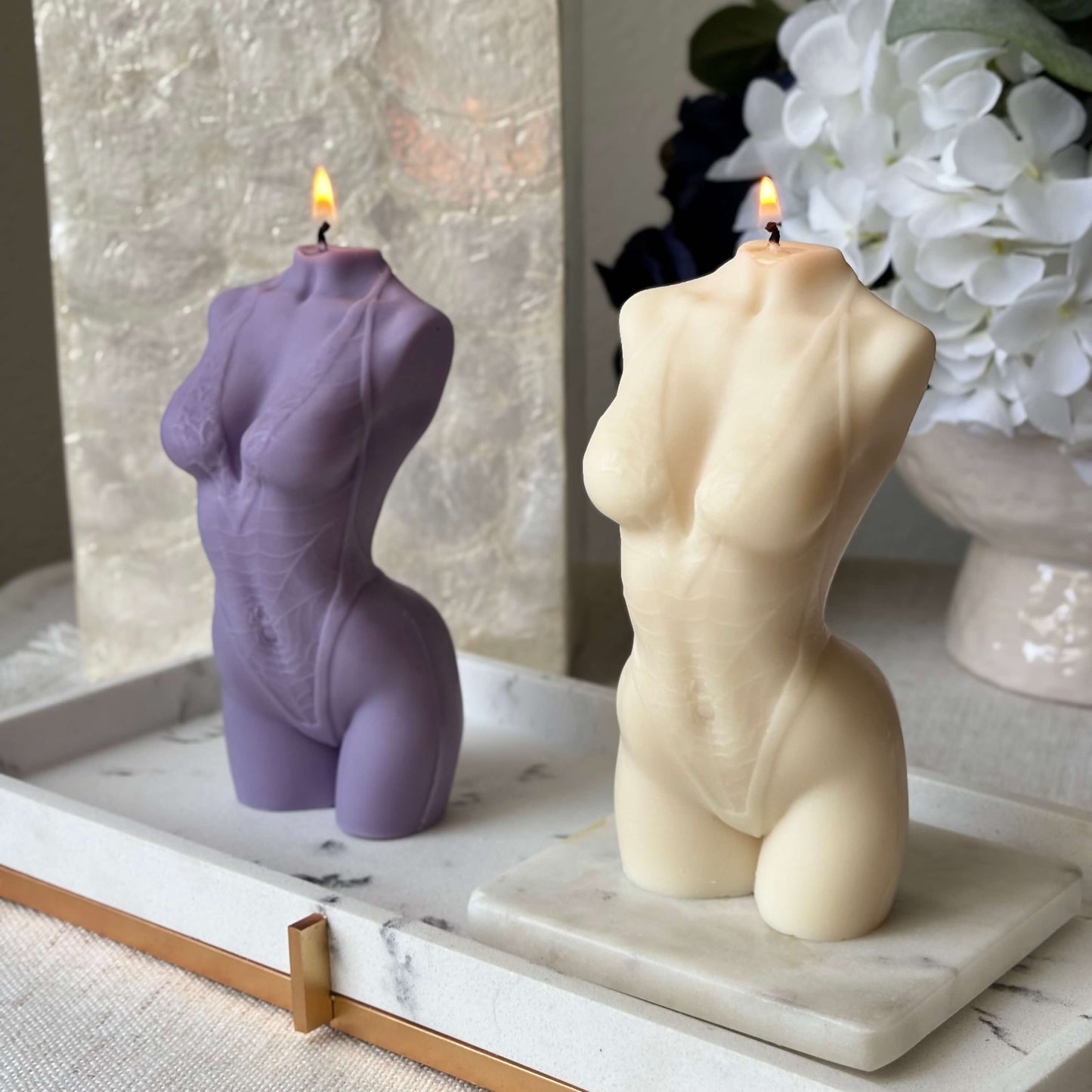 Two burning female torso candles, beige and purple soy wax sculptures, handmade decorative home décor.