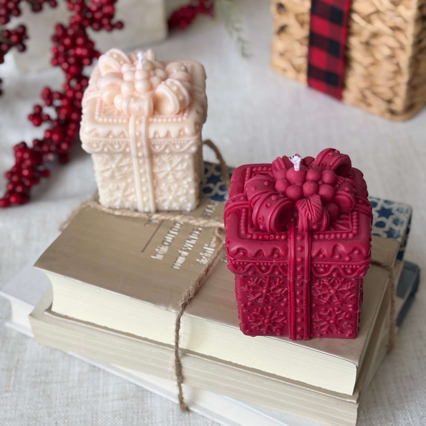 Red and beige gift box candles styled on stacked books with holiday berry decor.