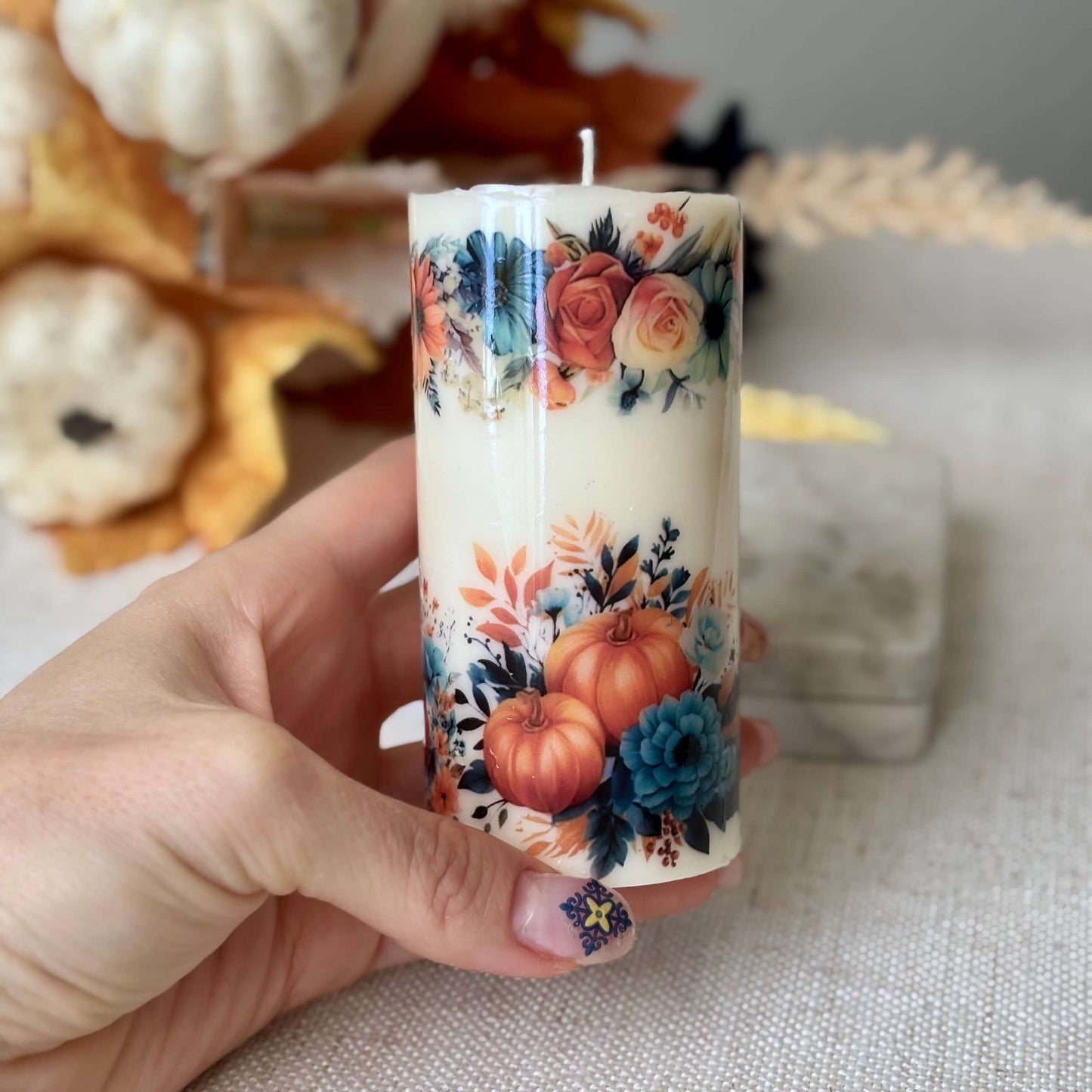 Handmade glossy pumpkin candle with floral autumn pattern held in hand