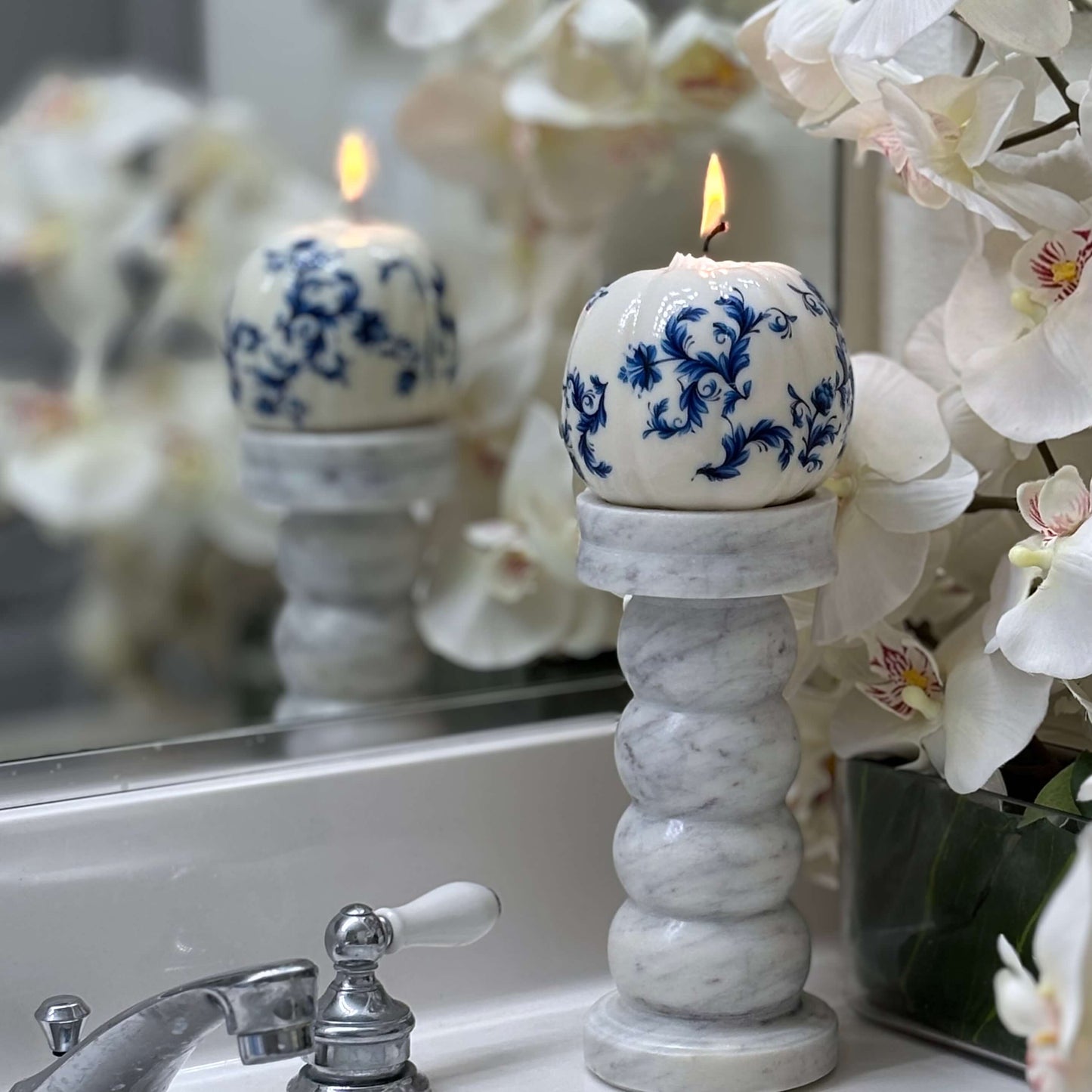 Blue and white pumpkin-shaped candle with baroque floral design, styled with orchids for Halloween and elegant seasonal decor.
