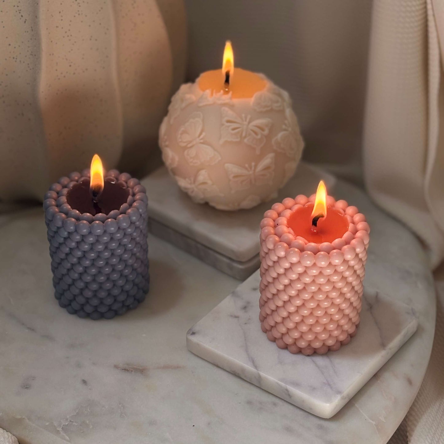 Burning handmade candles with pearl-like texture in neutral tones, set on stone base for calm interior styling.