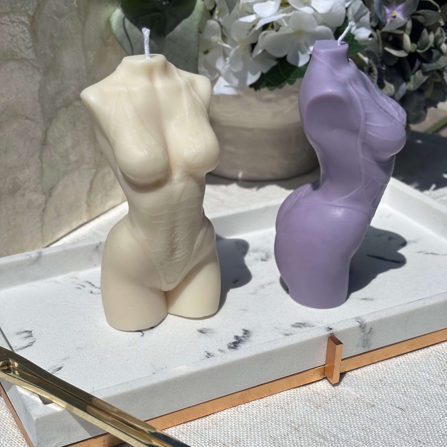Beige and purple female torso candles, soy wax body sculpture décor on marble tray with flowers.