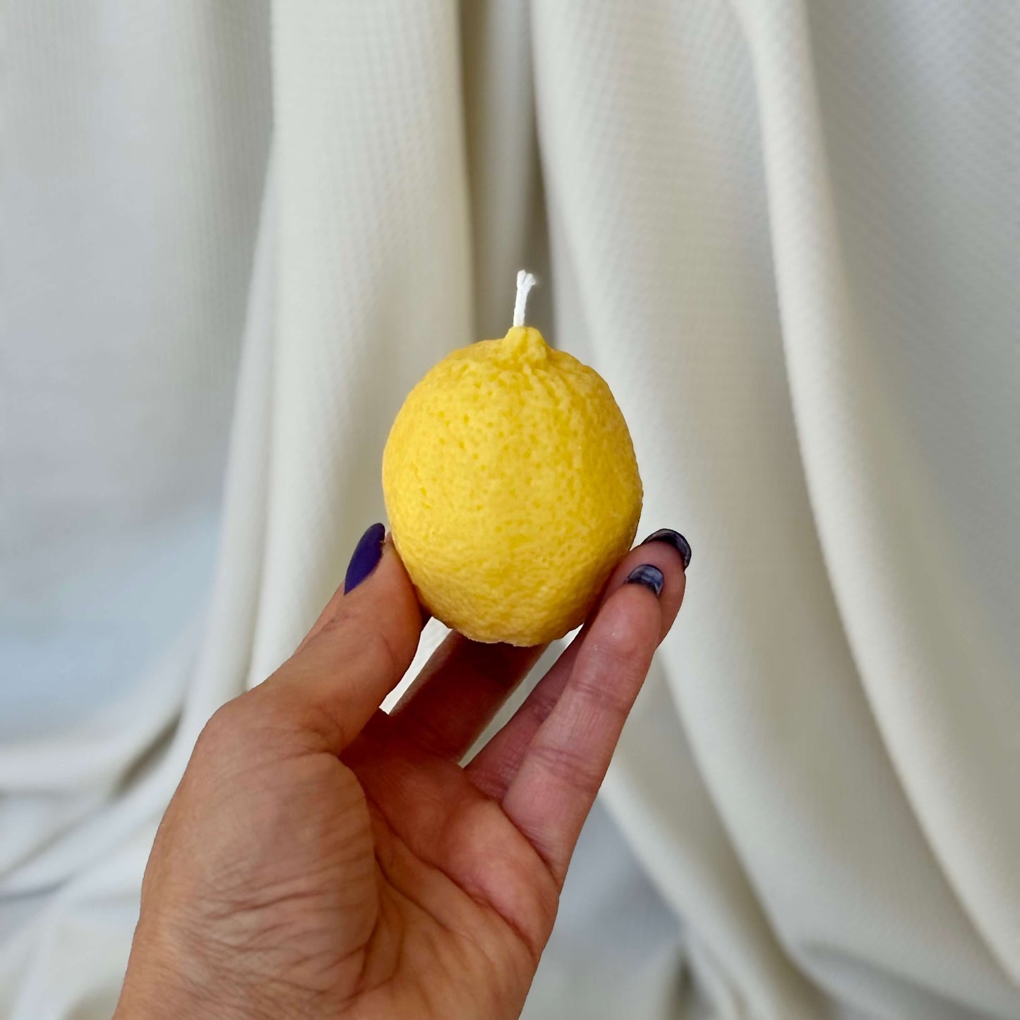 Close-up of hand holding vertical lemon candle. Fruit-shaped soy wax candle ideal for gifting.