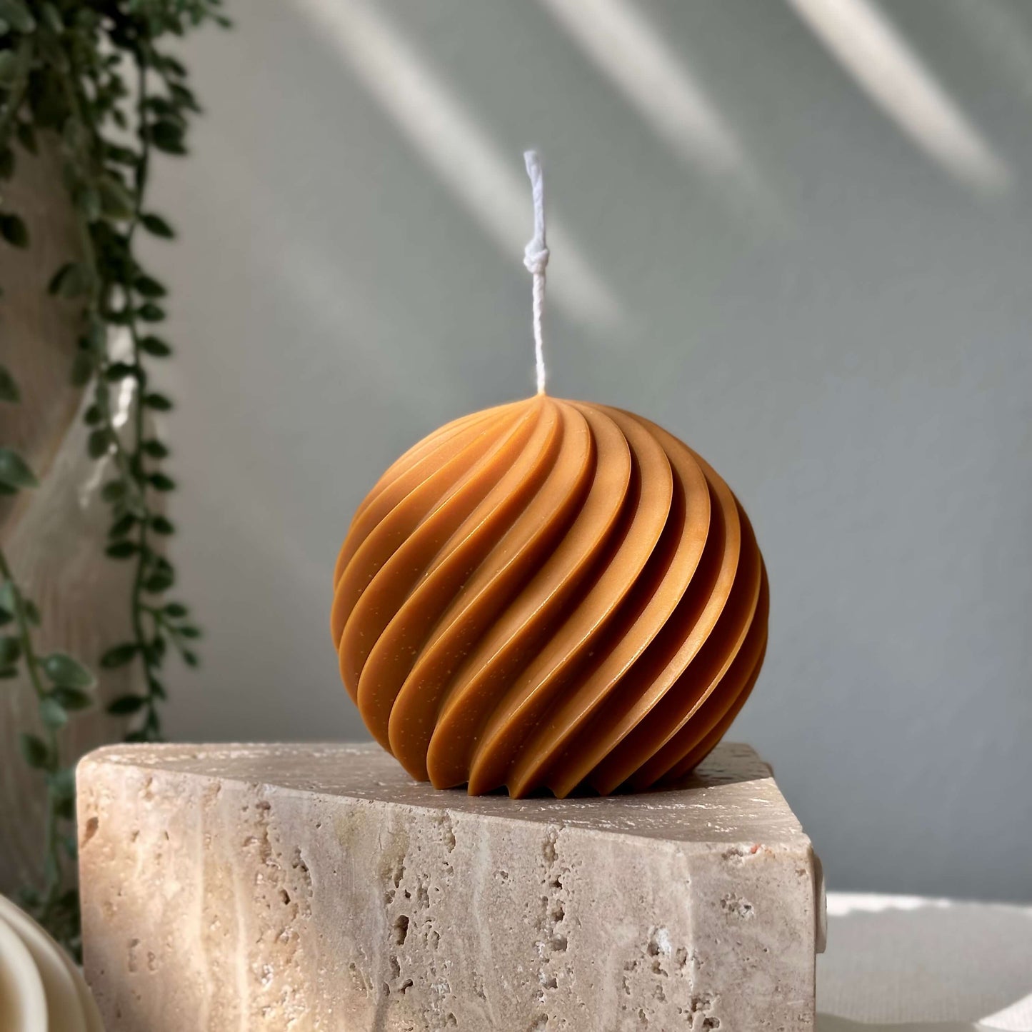 Honey brown spiral ball soy wax candle standing on a stone block with natural shadows, sculptural decorative accent.
