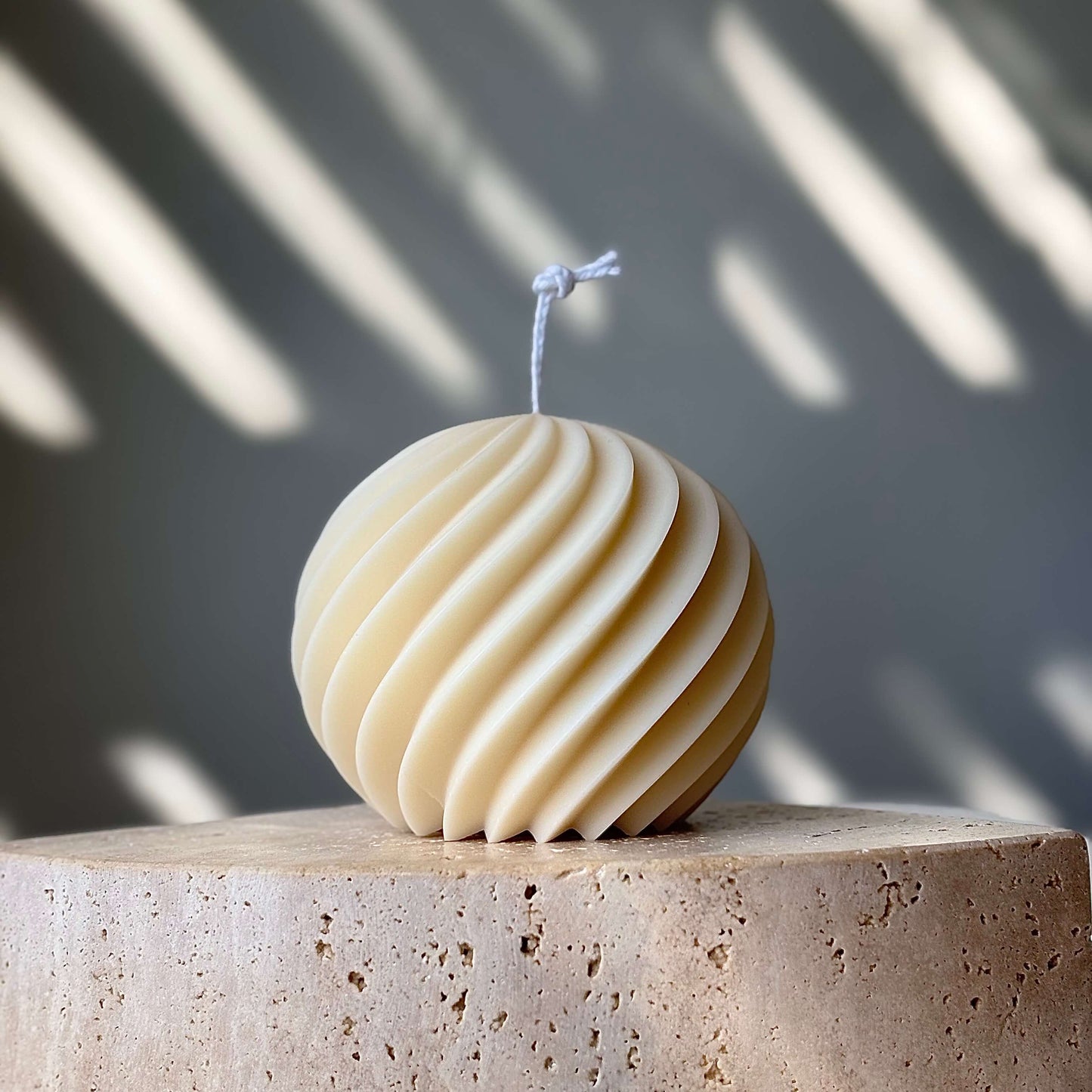 Ivory swirl ball soy wax candle placed on stone surface with shadow pattern, minimalist handmade decorative piece.