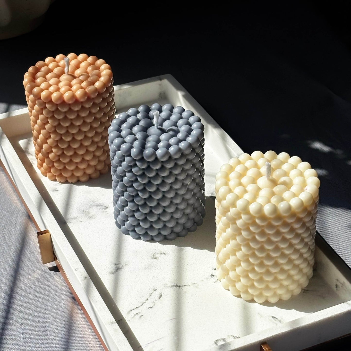 Sun-kissed soy wax candles in latte, creamy ivory, and slate blue — decorative pillars for shelf or relaxing space.