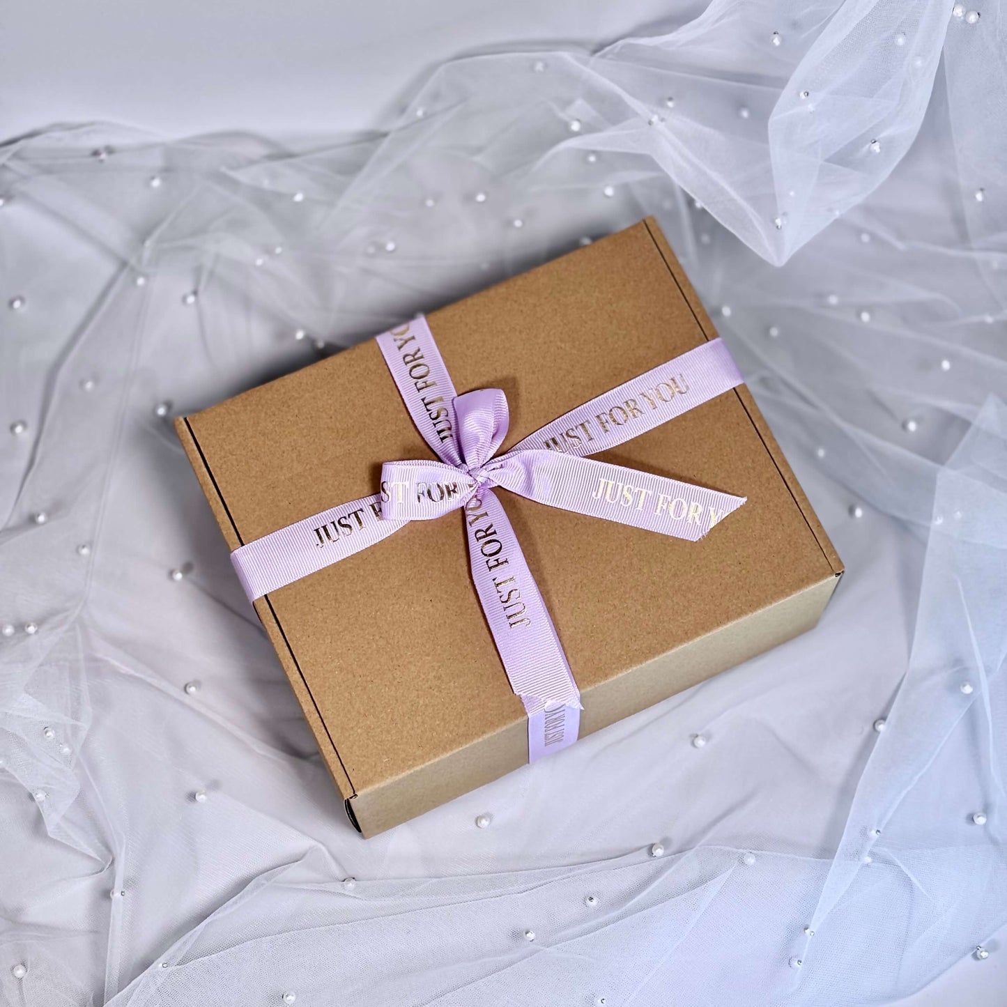 Closed lavender gift box tied with satin ribbon on soft white tulle background, ready for gifting