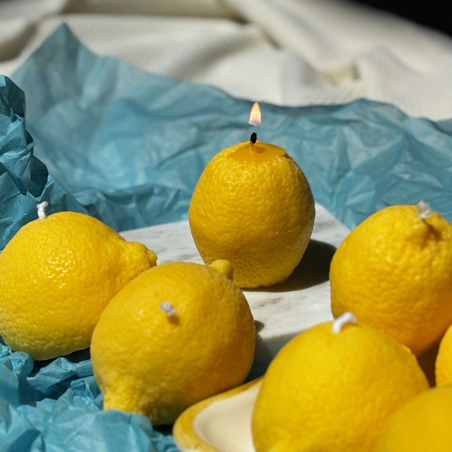 Lemon candle burning with other candles in background. Soy wax realistic citrus candle shown in use.
