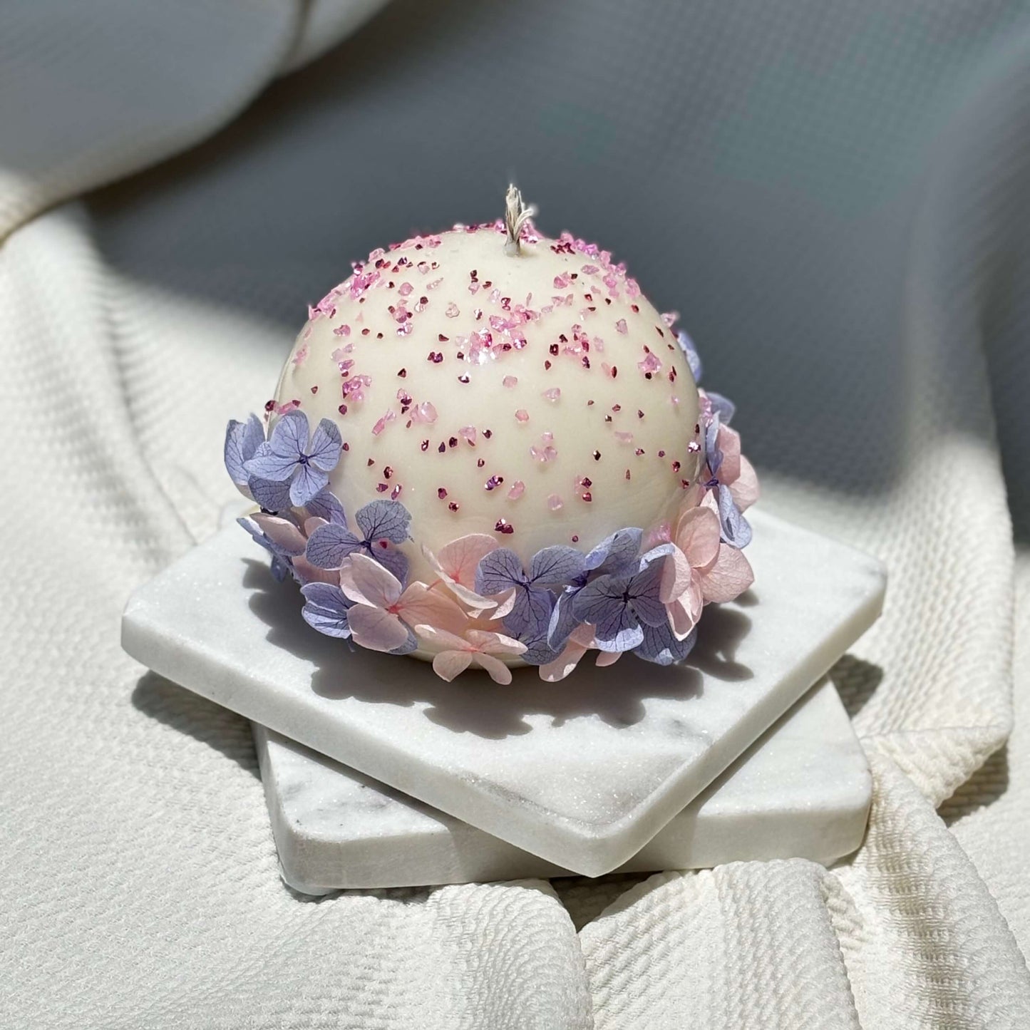 Luxurious handmade round candle with delicate flower details on elegant white marble tray