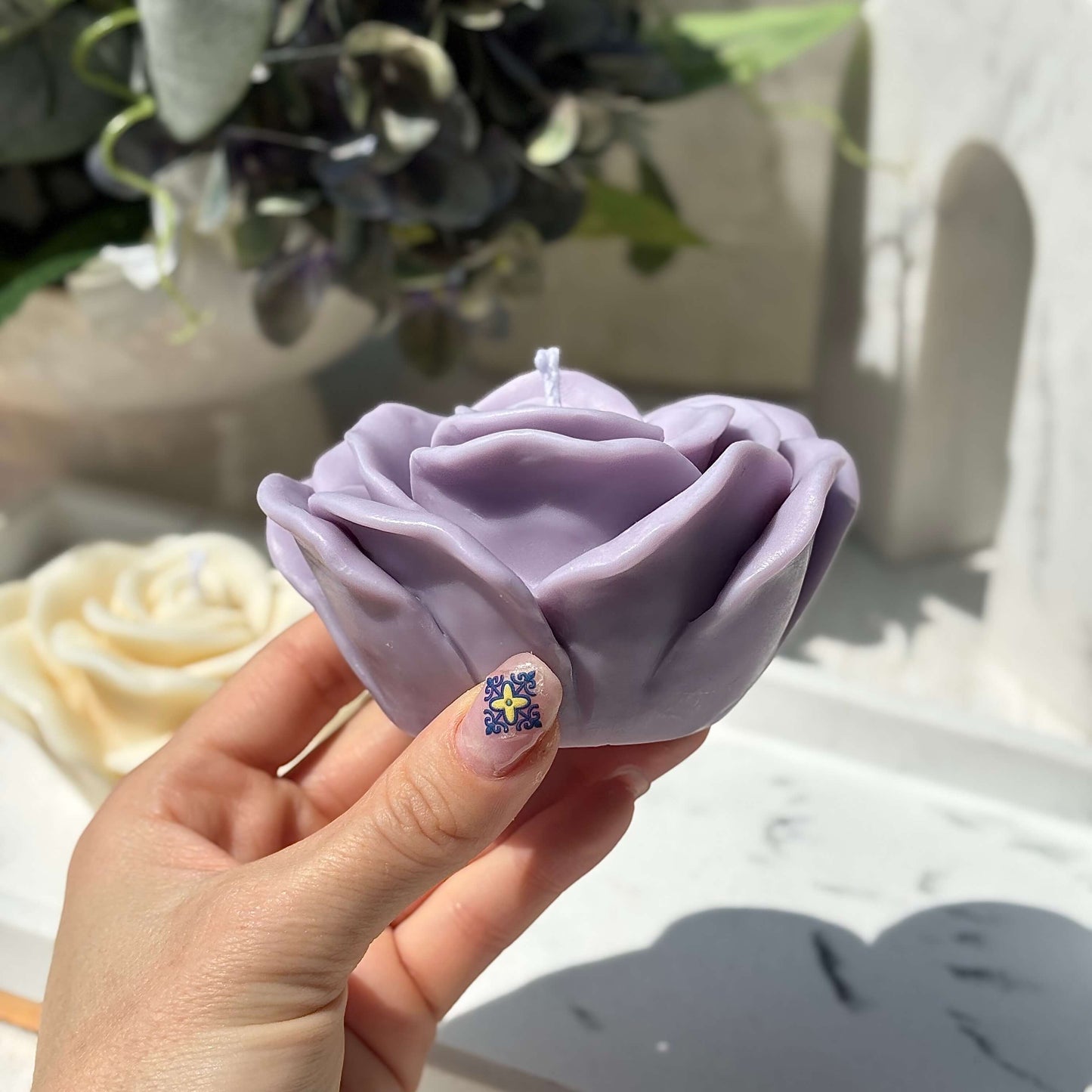 Hand holding handmade purple rose shaped candle crafted from soy wax