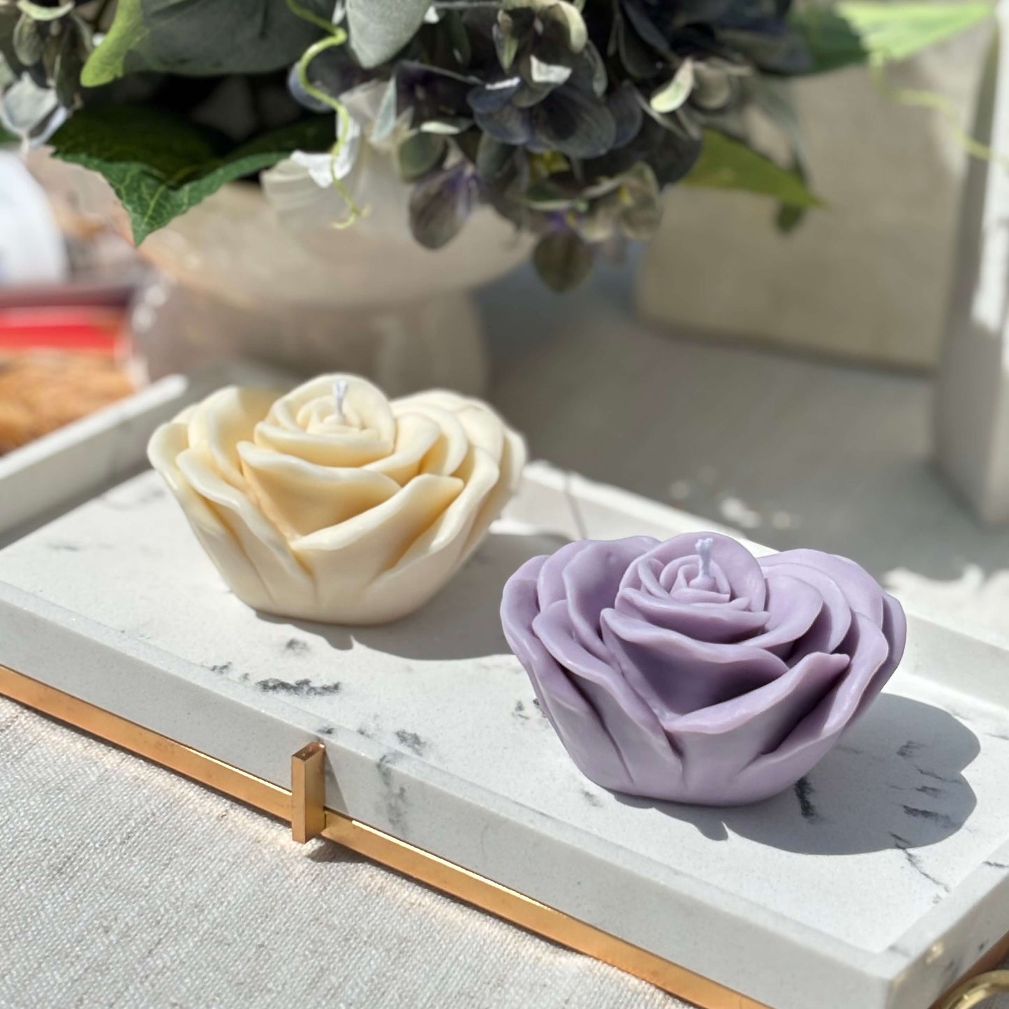 Two handmade rose shaped soy candles in purple and cream colors on marble tray for gift or decoration