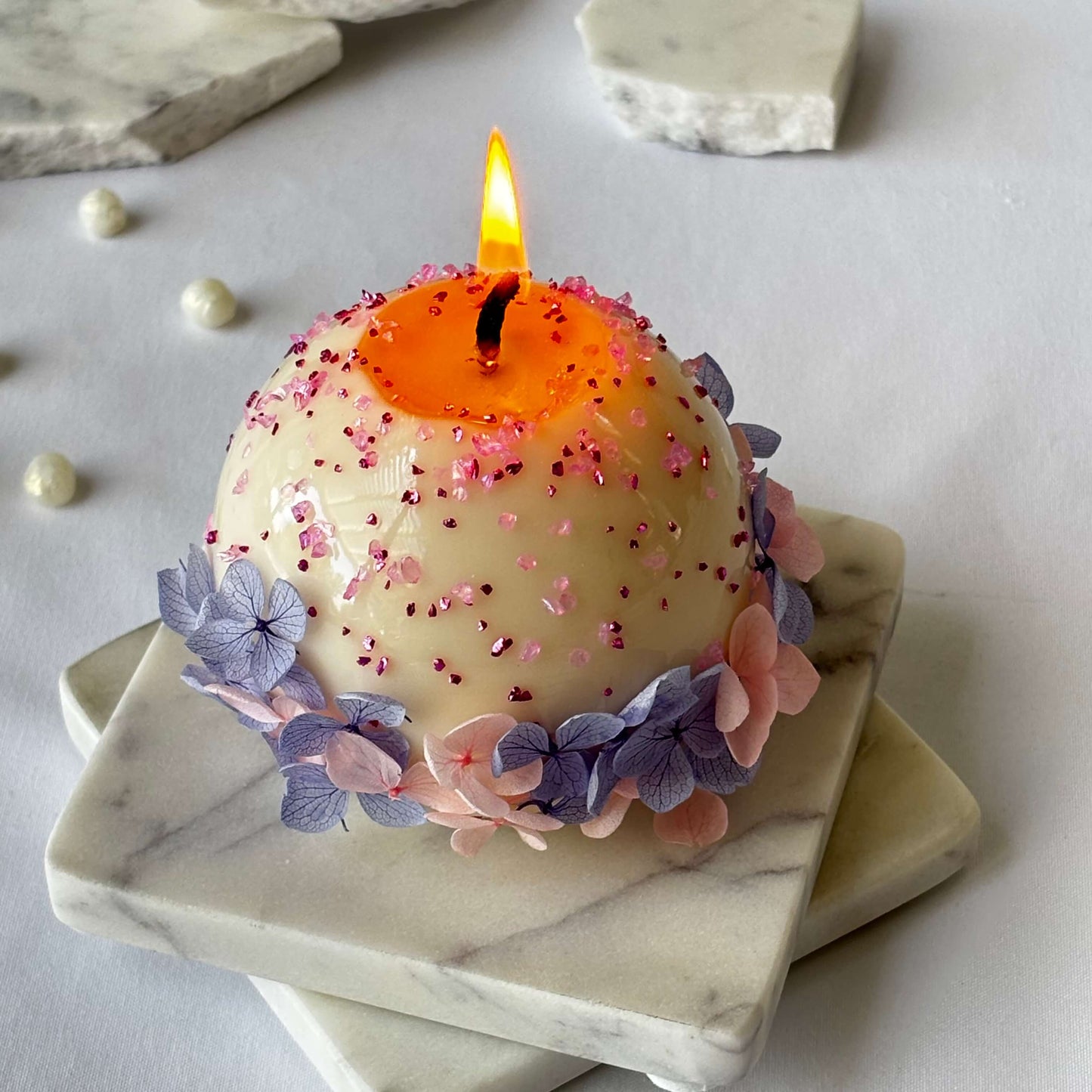 Handmade round candle with lilac and blush flowers burning on marble stand, luxury home decor