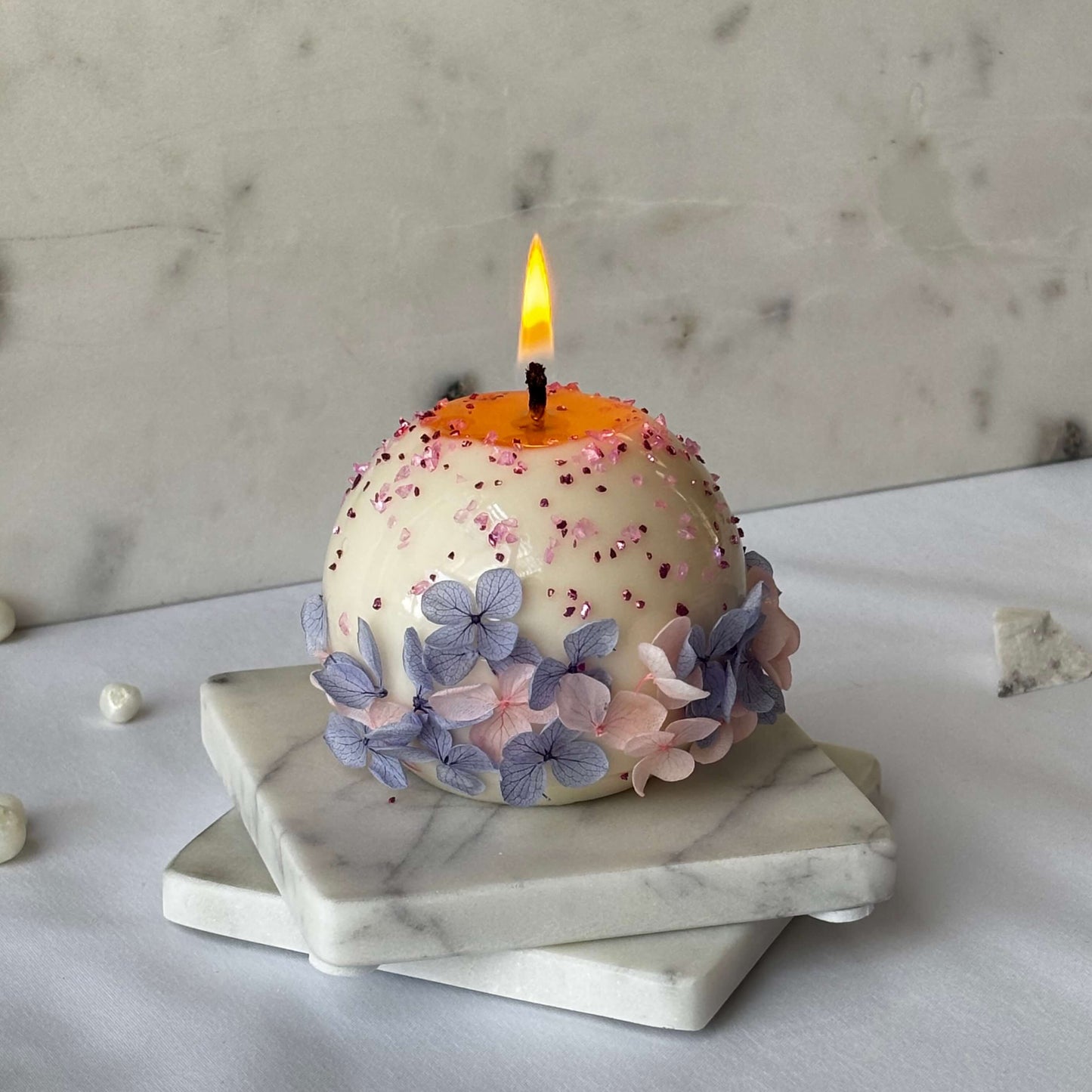 Lit round floral soy candle with pink sugar sprinkles and pastel petals on marble background