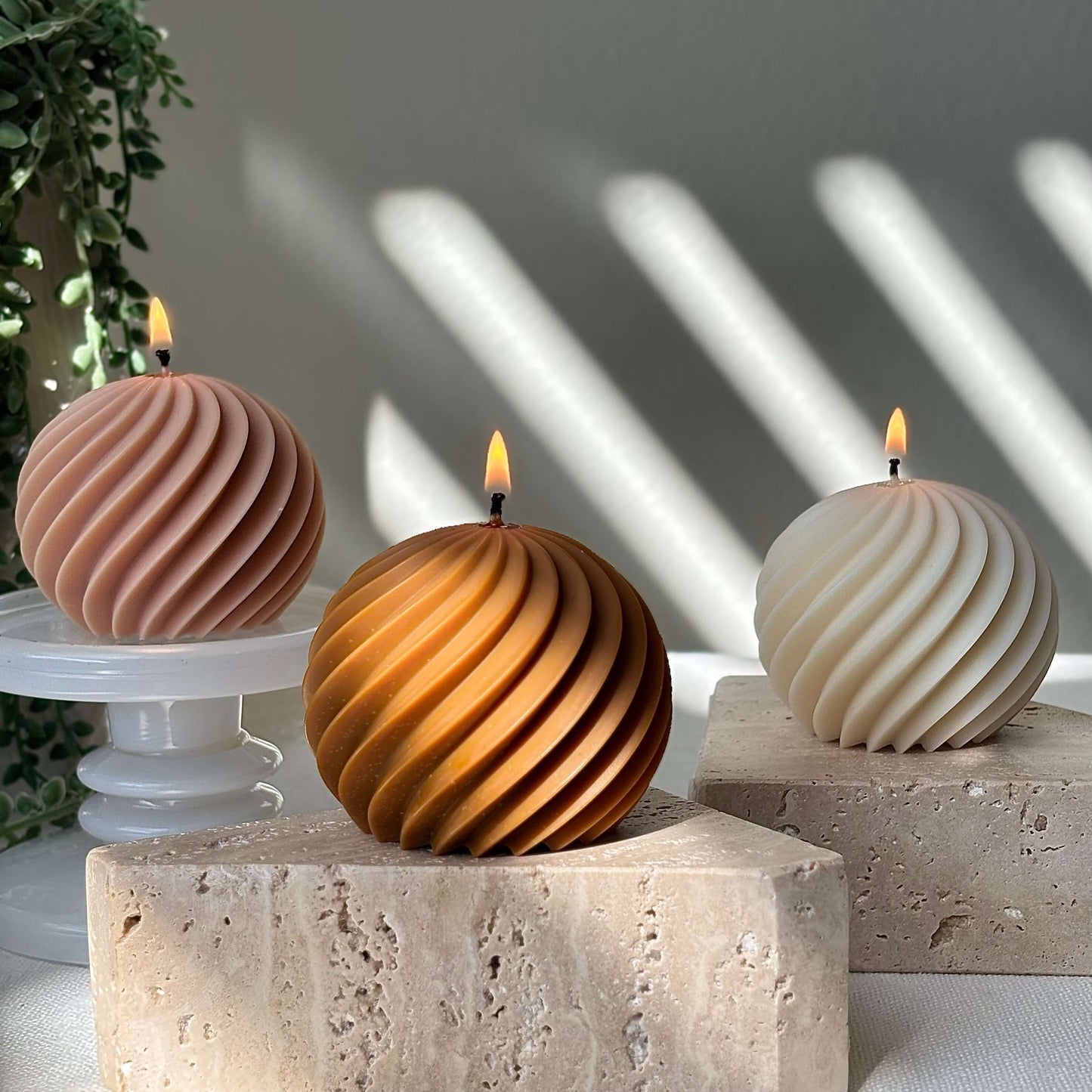 Three aesthetic swirl sphere candles burning on stone and white pedestals, handmade soy wax decor.
