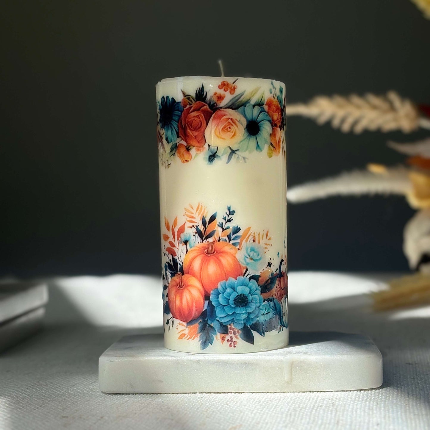 Shiny pumpkin candle with floral autumn design on marble base in warm light