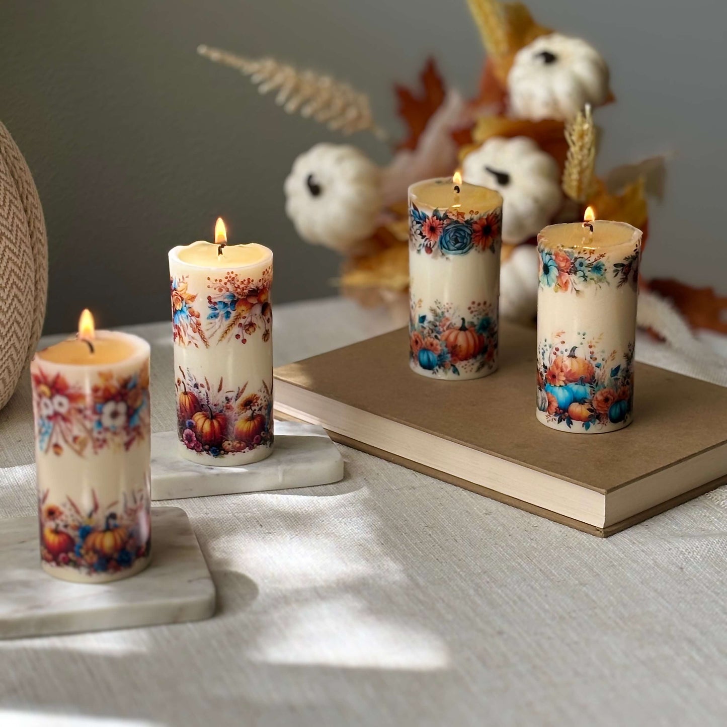 Three shiny pumpkin candles with floral autumn patterns glowing on table with seasonal decor