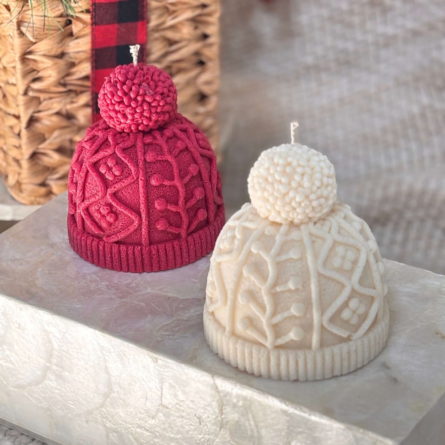 Pair of decorative candles shaped like knit hats in red and white displayed on a light marble surface for Thanksgiving or Christmas gift decor