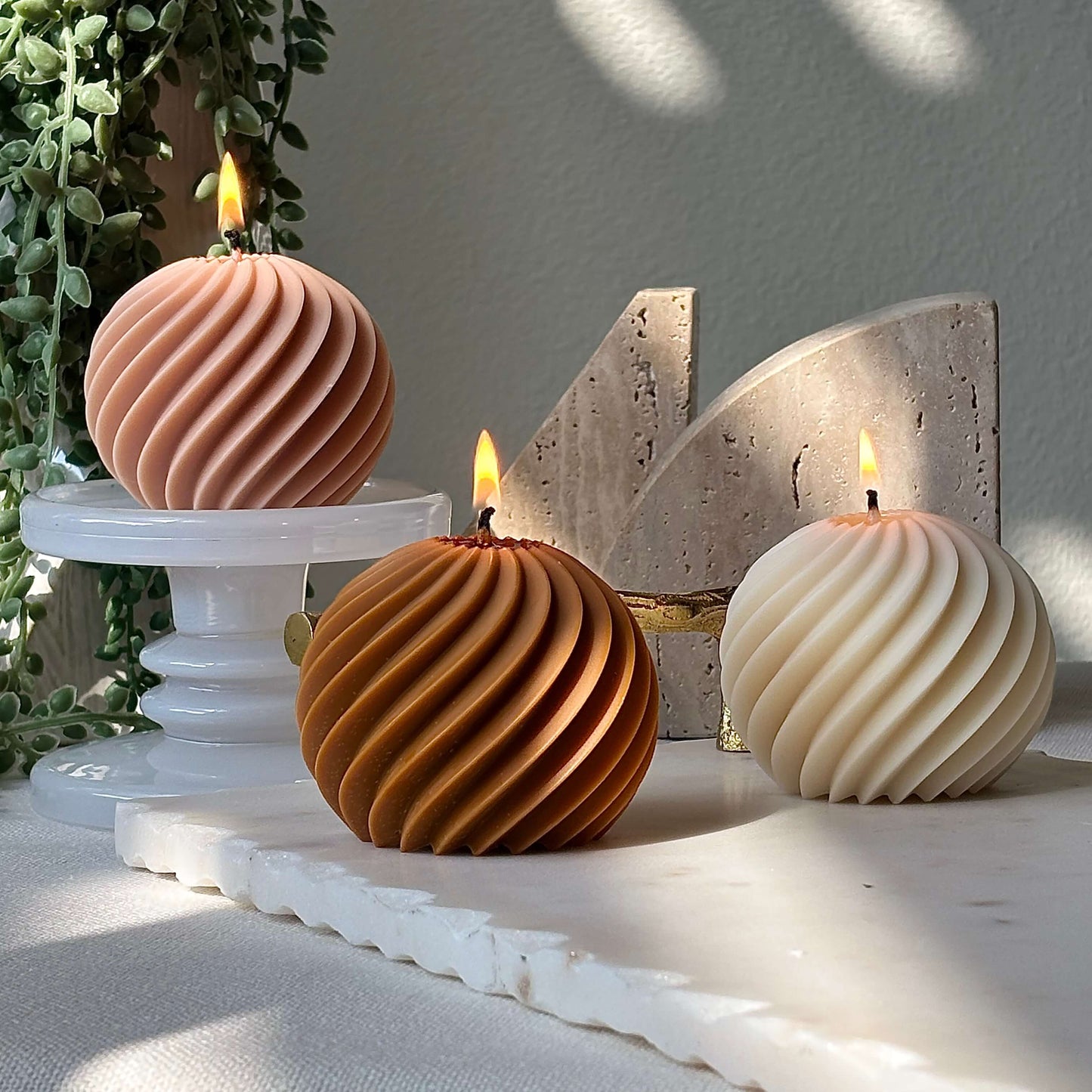 Handmade swirl soy wax candles burning in peach, ivory and honey tones on marble pedestals, elegant sculptural gift decor.