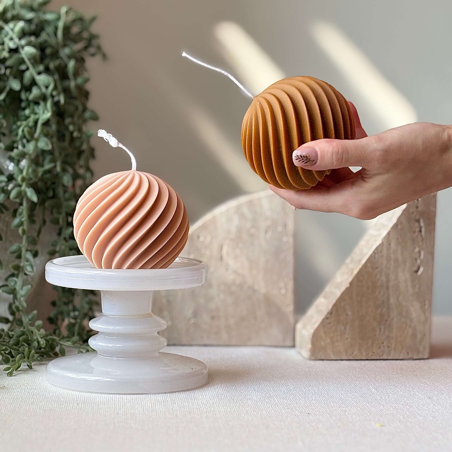 Two swirl ball candles in peach and honey color on marble pedestals, minimalist handmade decor accent.