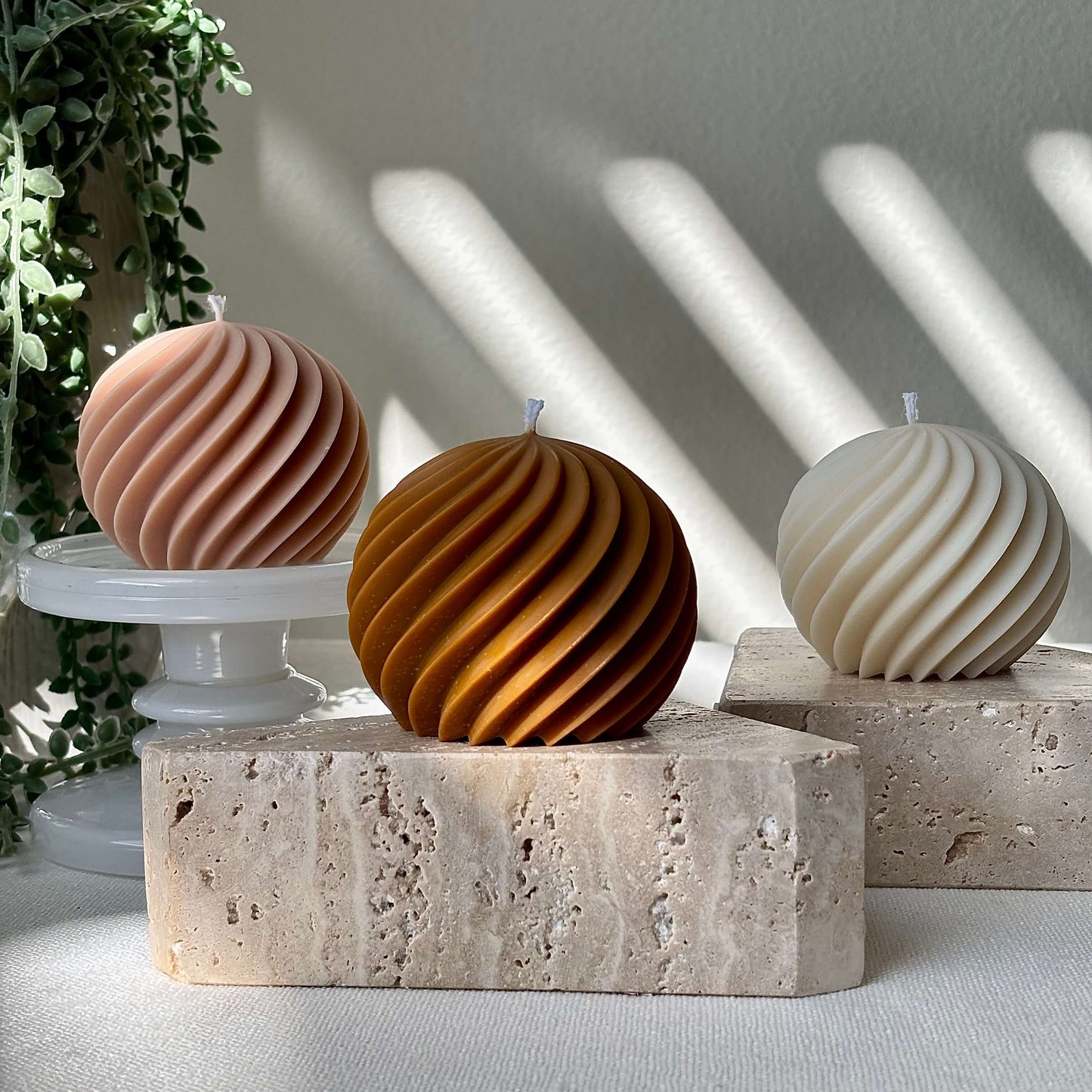 Three spiral soy wax candles on stone bases with plant background, modern handmade gift candles for home decor.