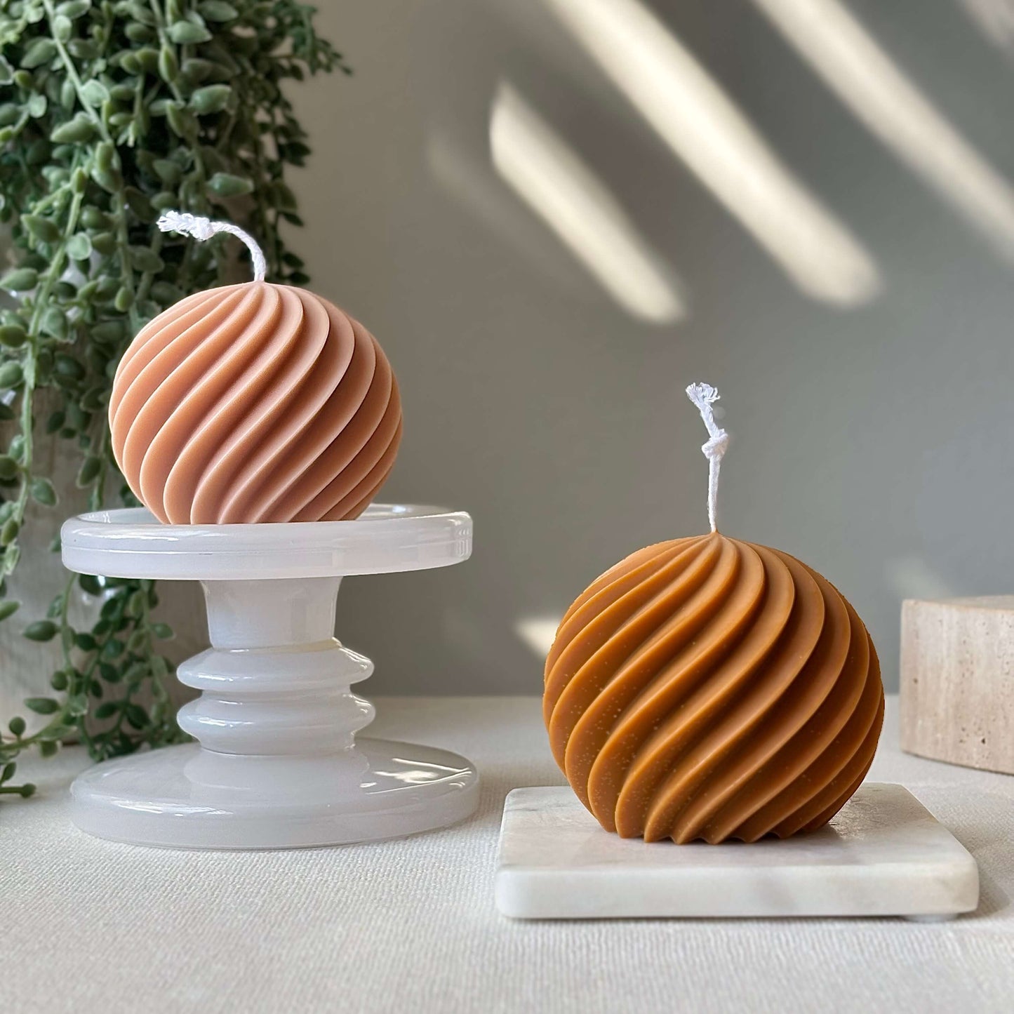 Two sculptural swirl sphere candles in peach and honey on marble stands with soft light, handmade aesthetic candle gift.