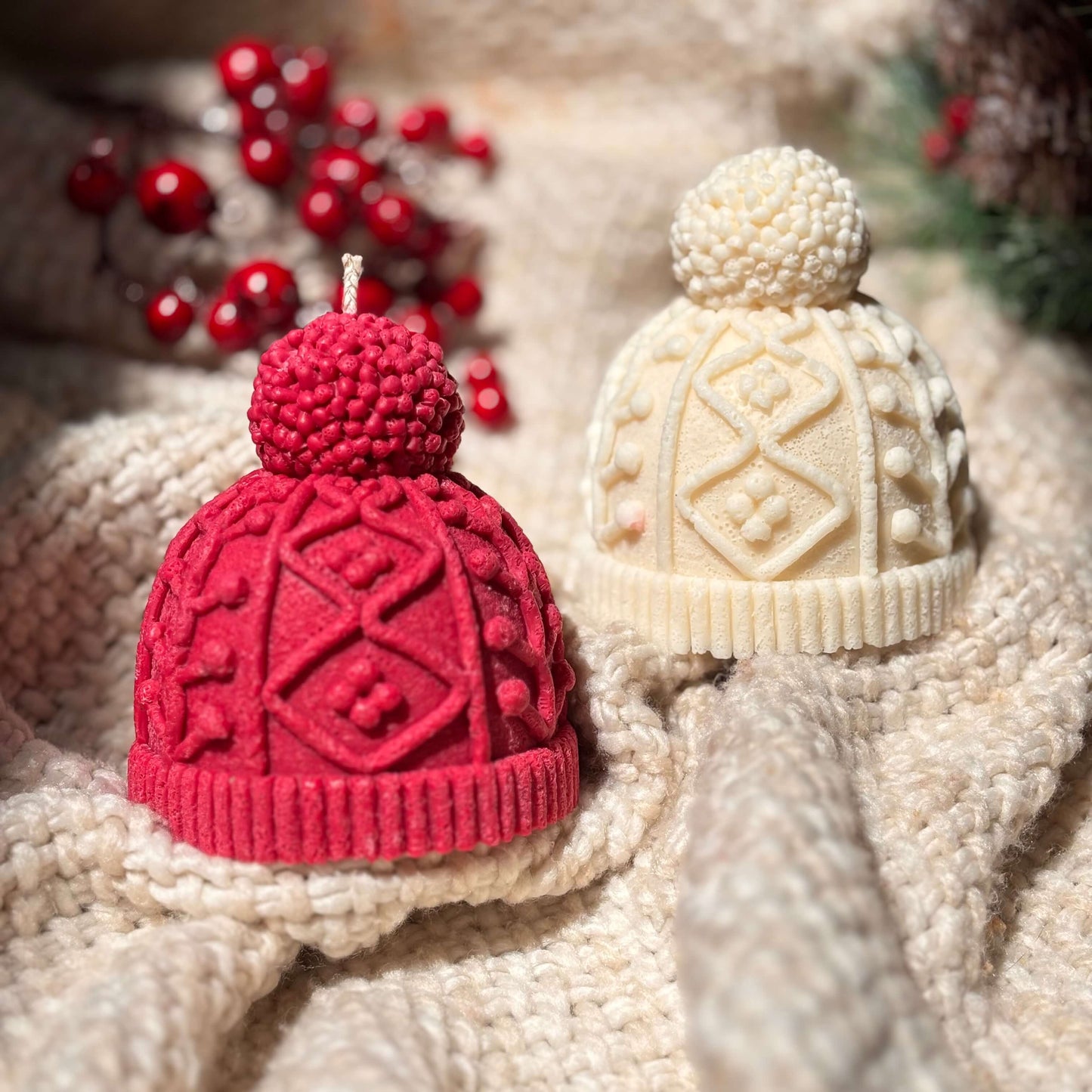Textured soy candles in red and cream shaped like knitted hats styled on soft fabric with festive berries for Thanksgiving or Secret Santa gifts