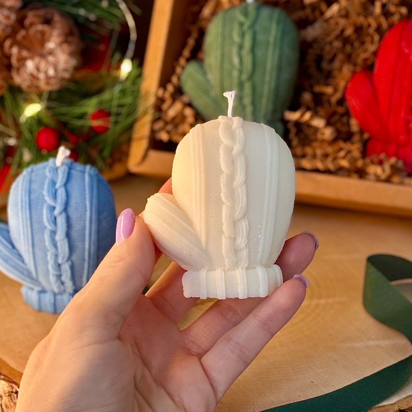 White mitten candle in hand with cozy Christmas gift box in background for holiday aesthetic