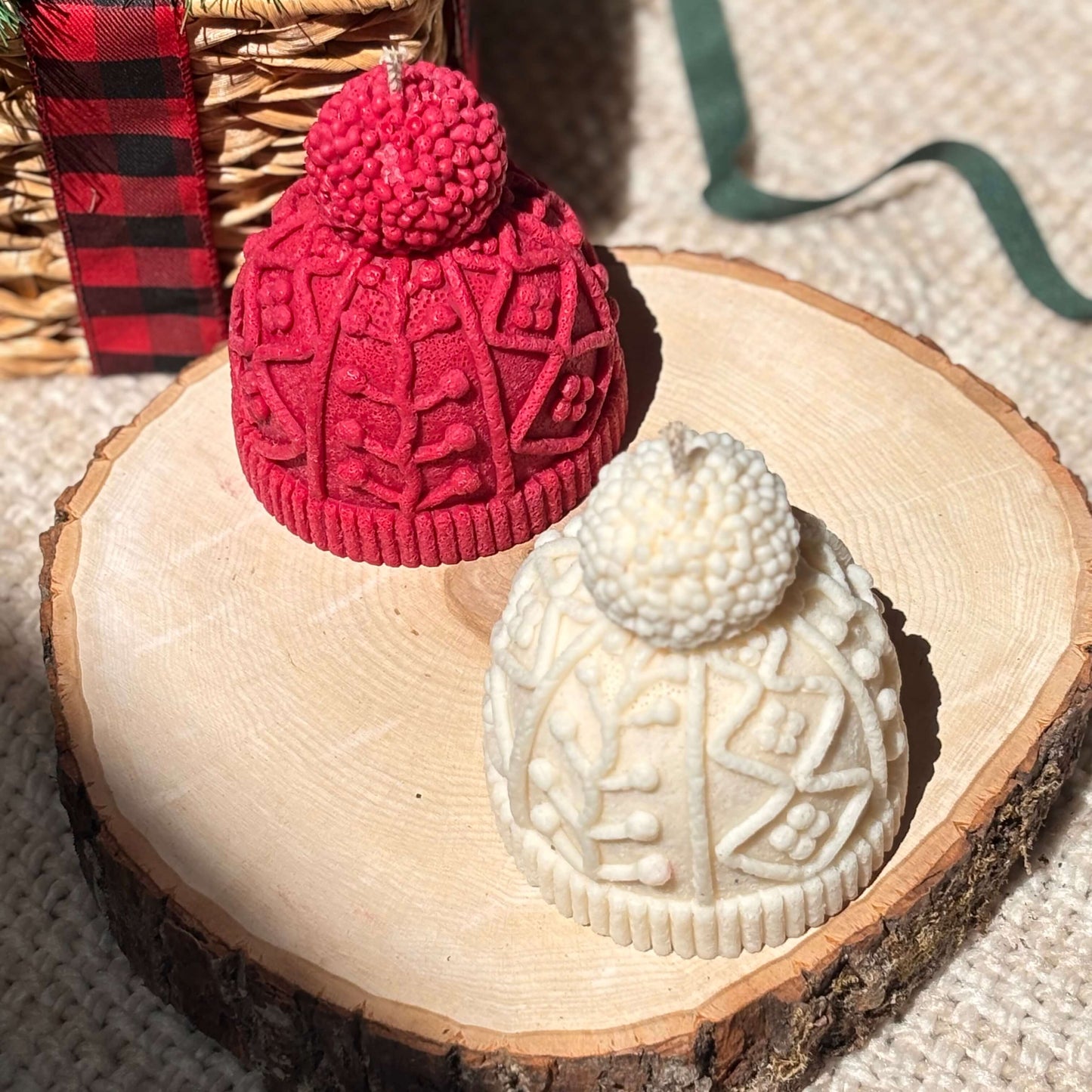 Winter knit hat candles in red and off-white placed on raw wood slice with rustic background, styled as woodland-inspired Christmas or hostess gift