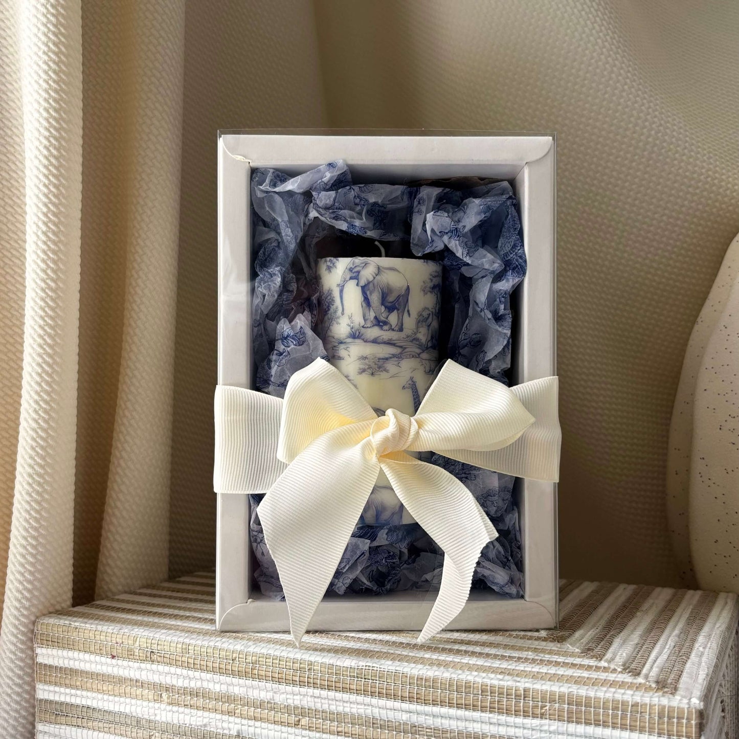 Hand-poured candle in blue and cream safari style, presented in luxury gift box with ribbon, styled against minimalist striped decor.