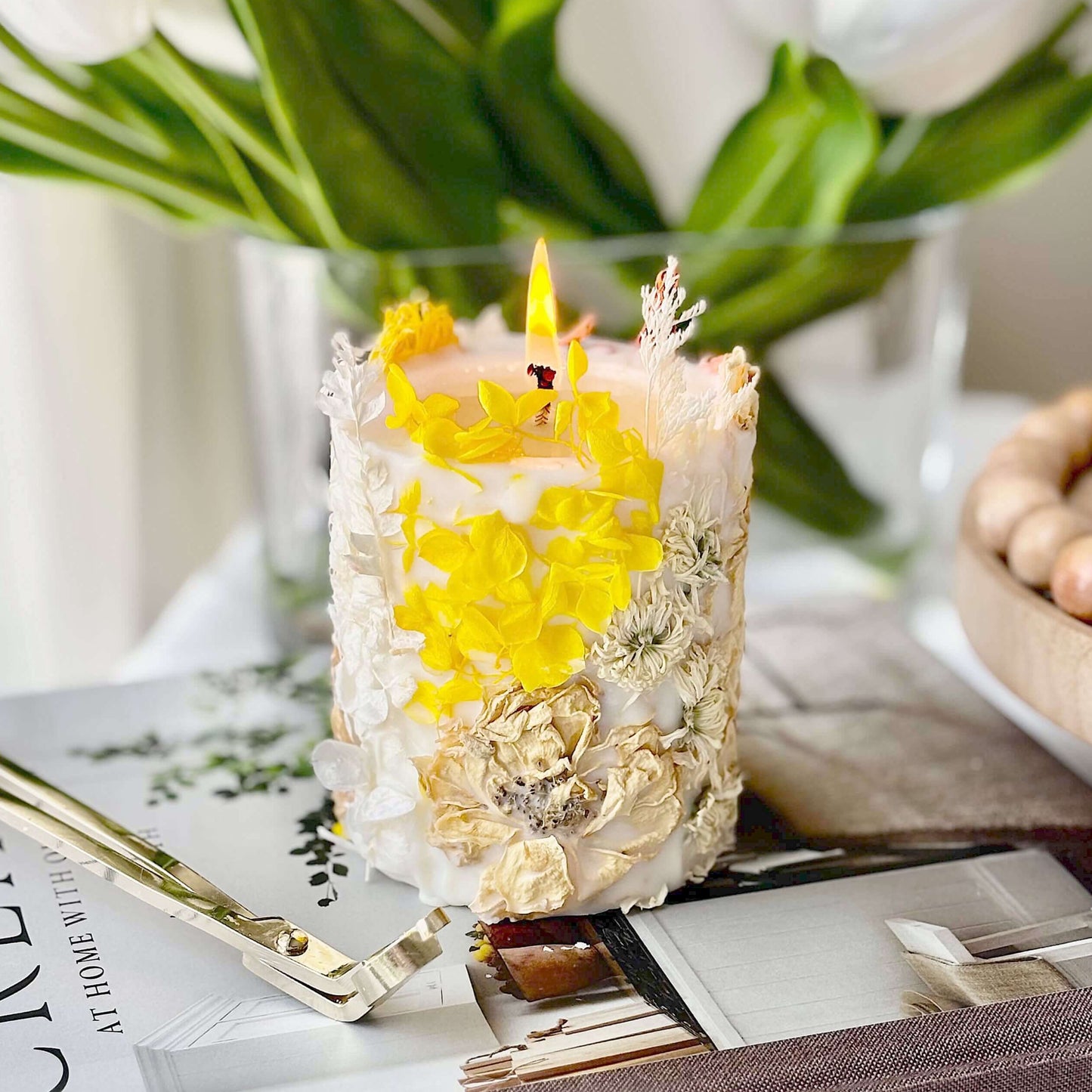 Handmade botanical soy candle with pressed yellow flowers, burning on a table. Elegant home decor made in California.