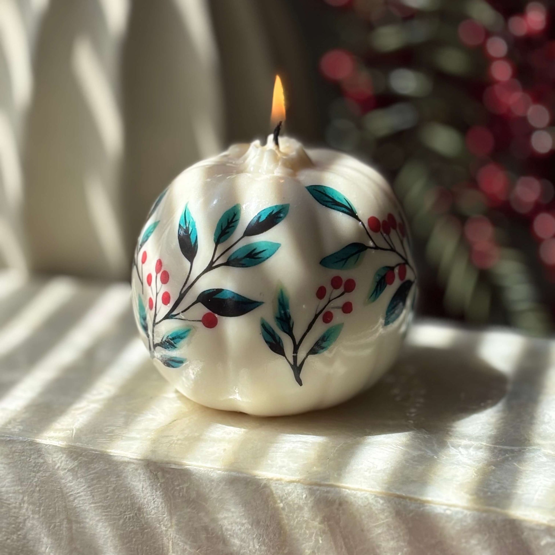 Glossy floral pumpkin candle with teal leaves and red berries burning on a marble surface, perfect as Halloween home accent, fall decor or Thanksgiving hostess gift

